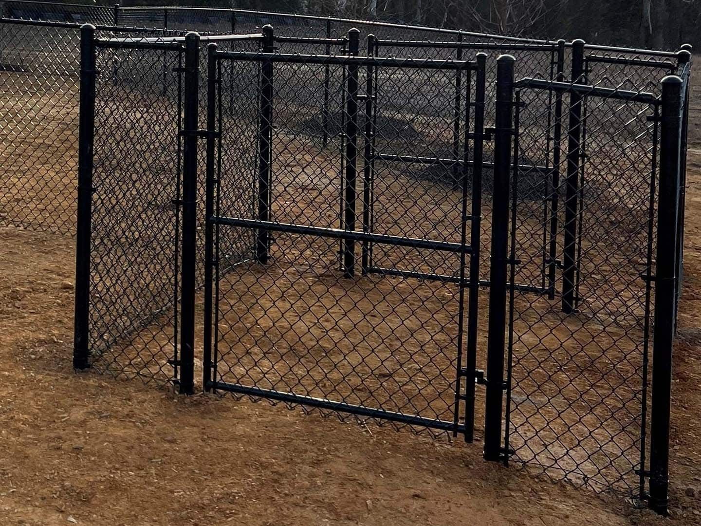 Black chain-link fence enclosure with gates on a dirt ground.