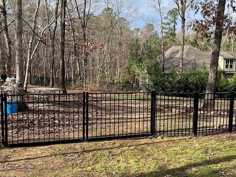 Black metal fence in front of a wooded area and house.