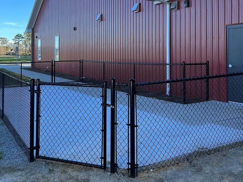 Black chain-link fence encloses a concrete patio next to a burgundy building with a black door.