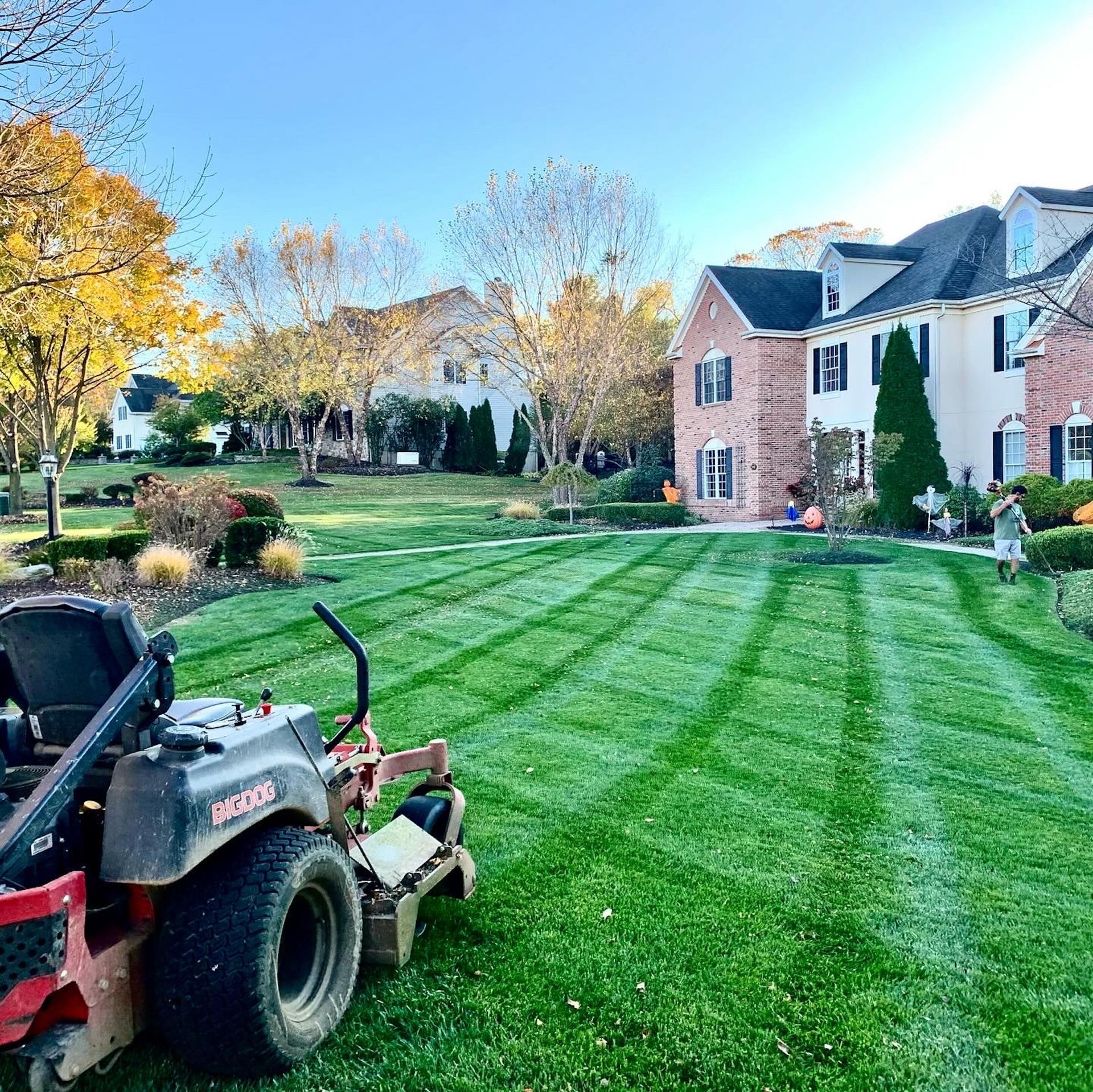 Lawnmower on a freshly cut lawn in front of a large house on a sunny day.