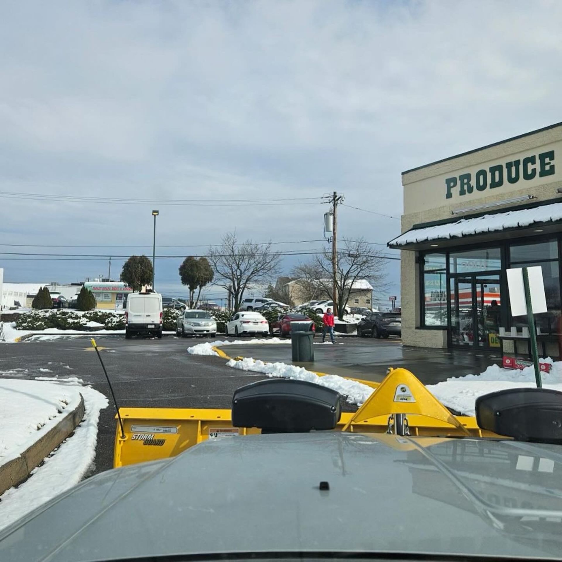 Snowplow clearing a parking lot in front of a produce store on a snowy day.