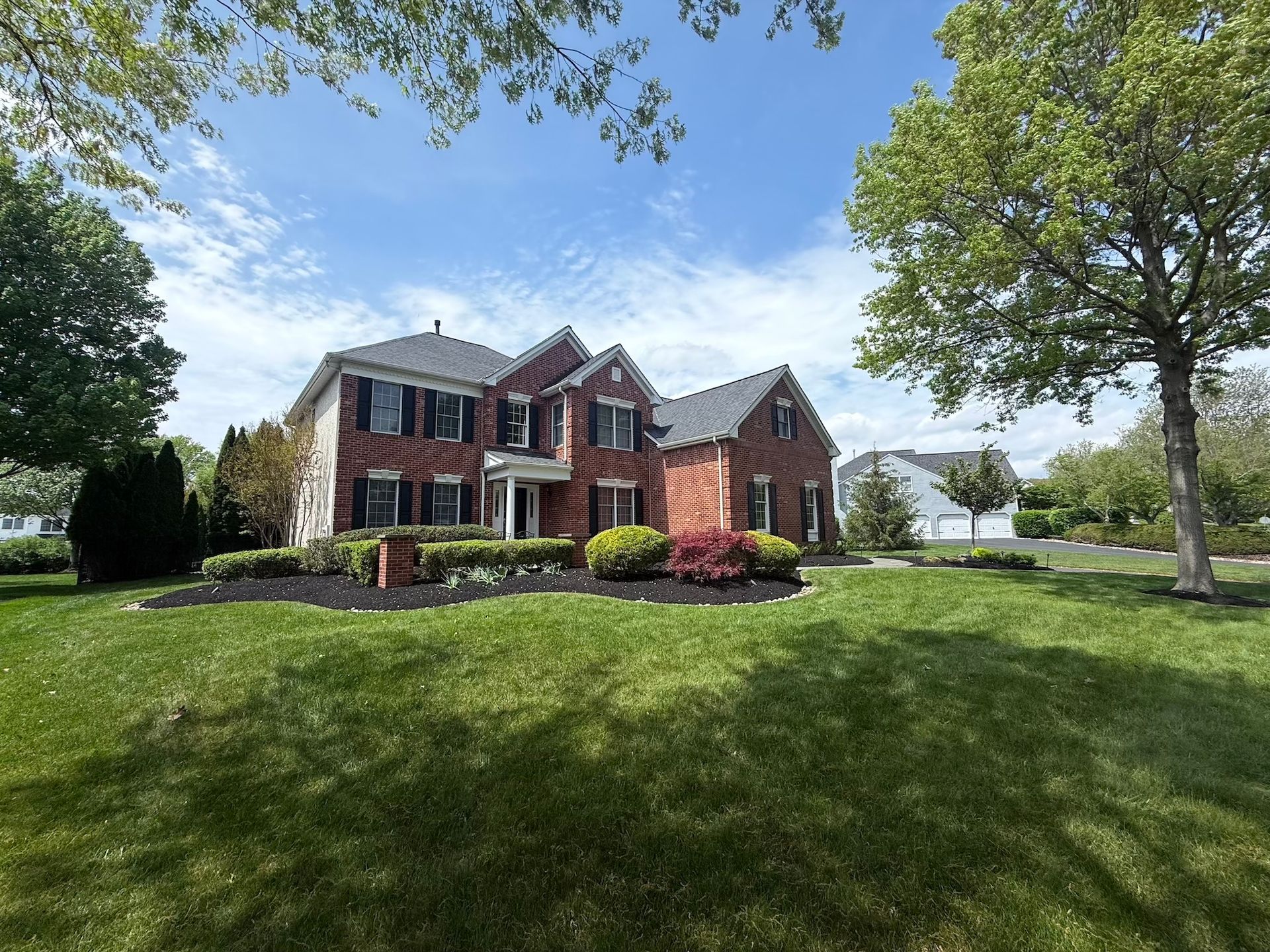 Two-story brick house with black shutters, green lawn, and blue sky.