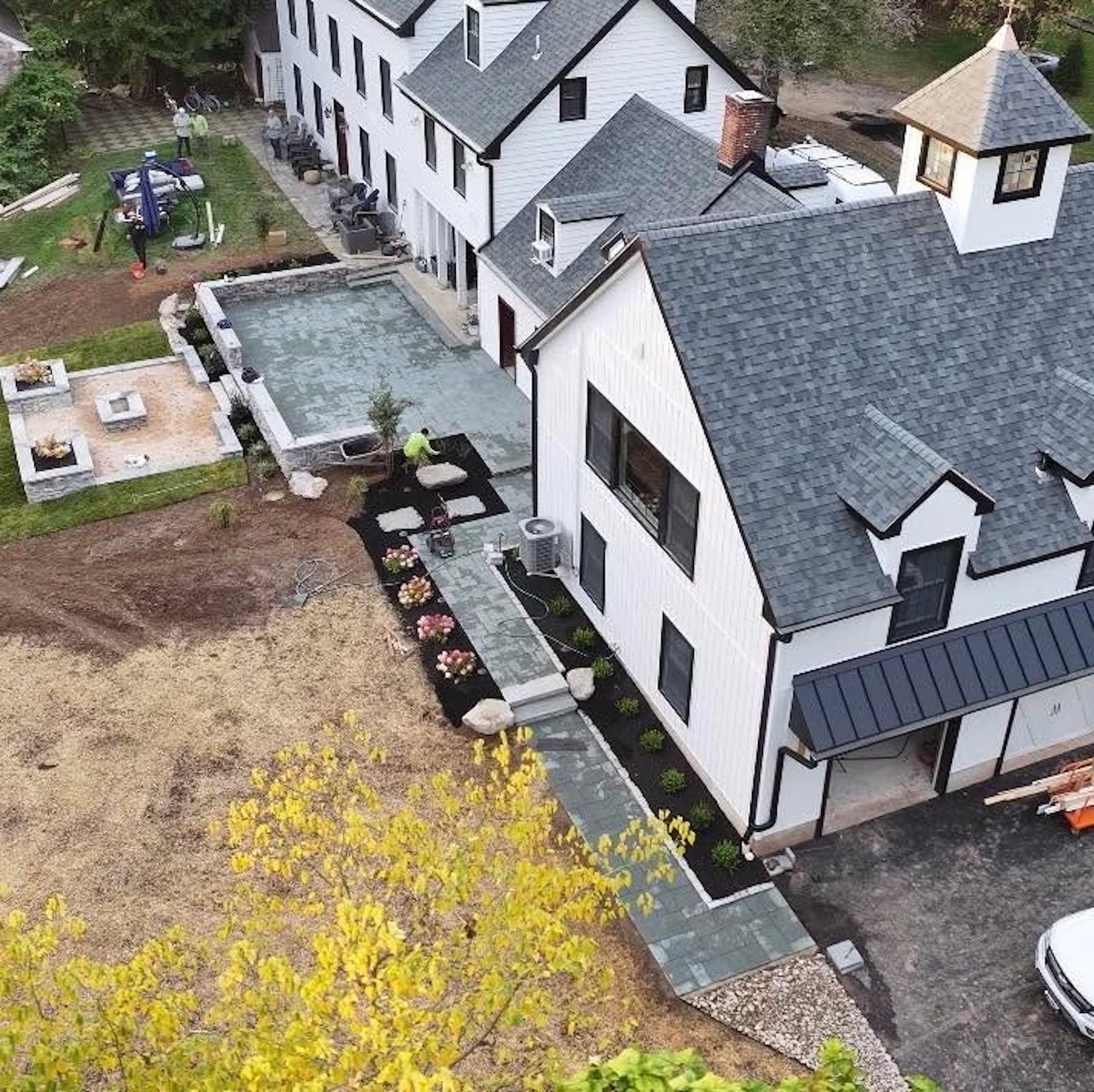 Aerial view of a white house with a dark gray roof and surrounding landscaping with patio and fire pit.