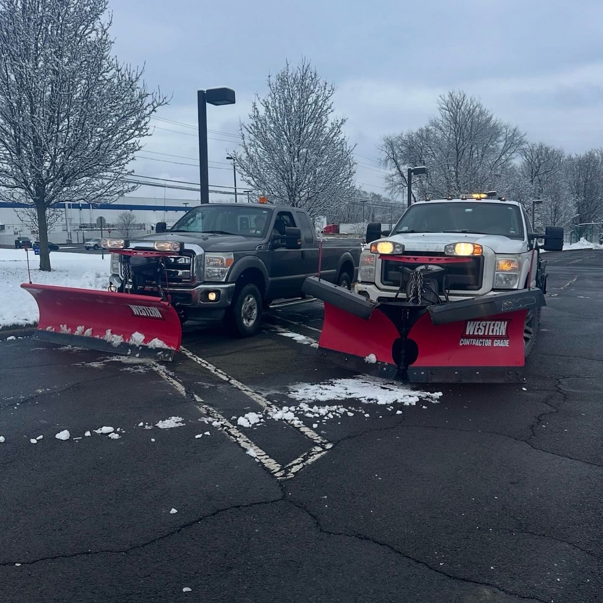 Two snowplow trucks clearing snow in a parking lot.
