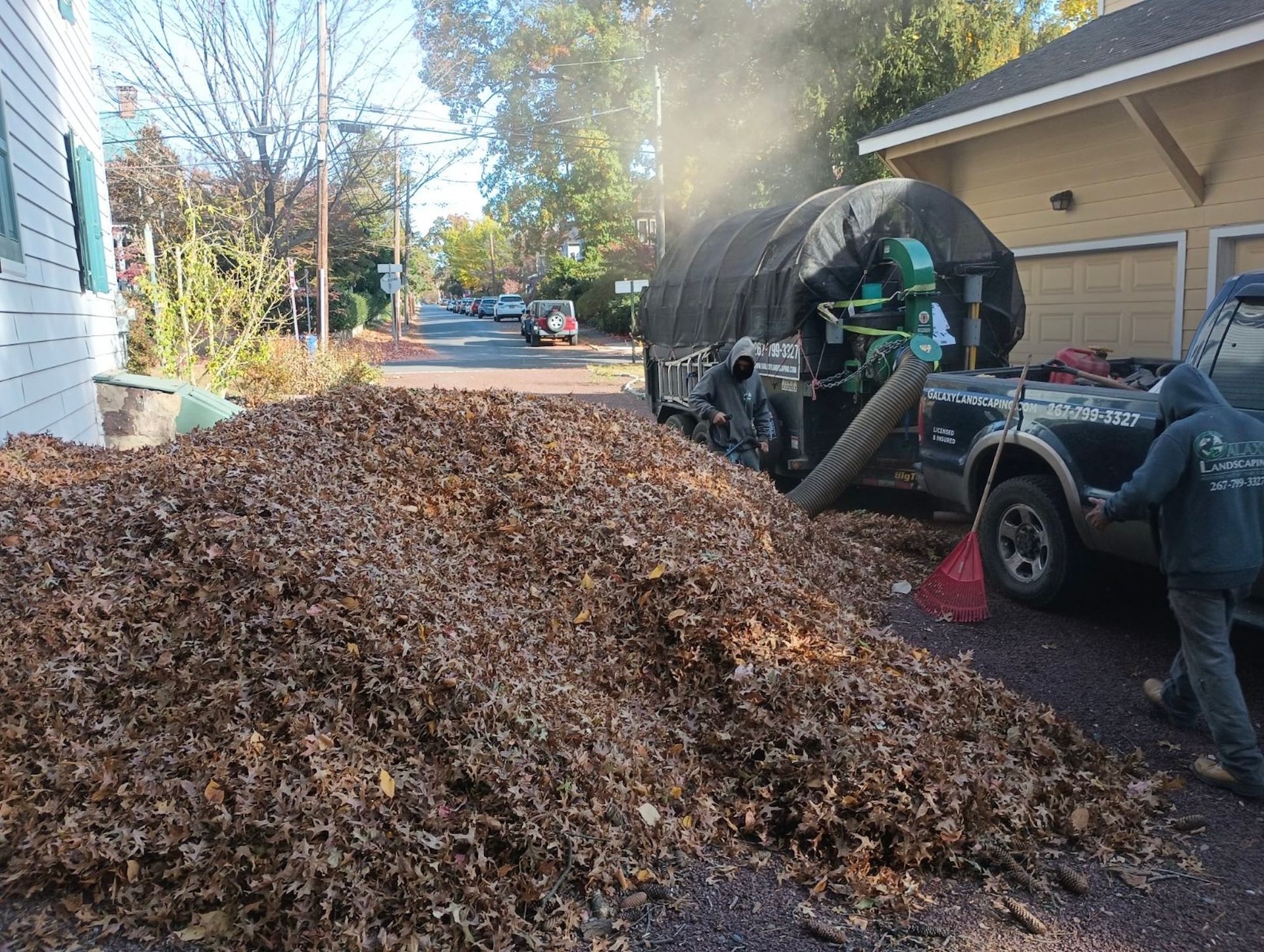 A large pile of leaves being vacuumed into a truck-mounted leaf collector on a driveway.