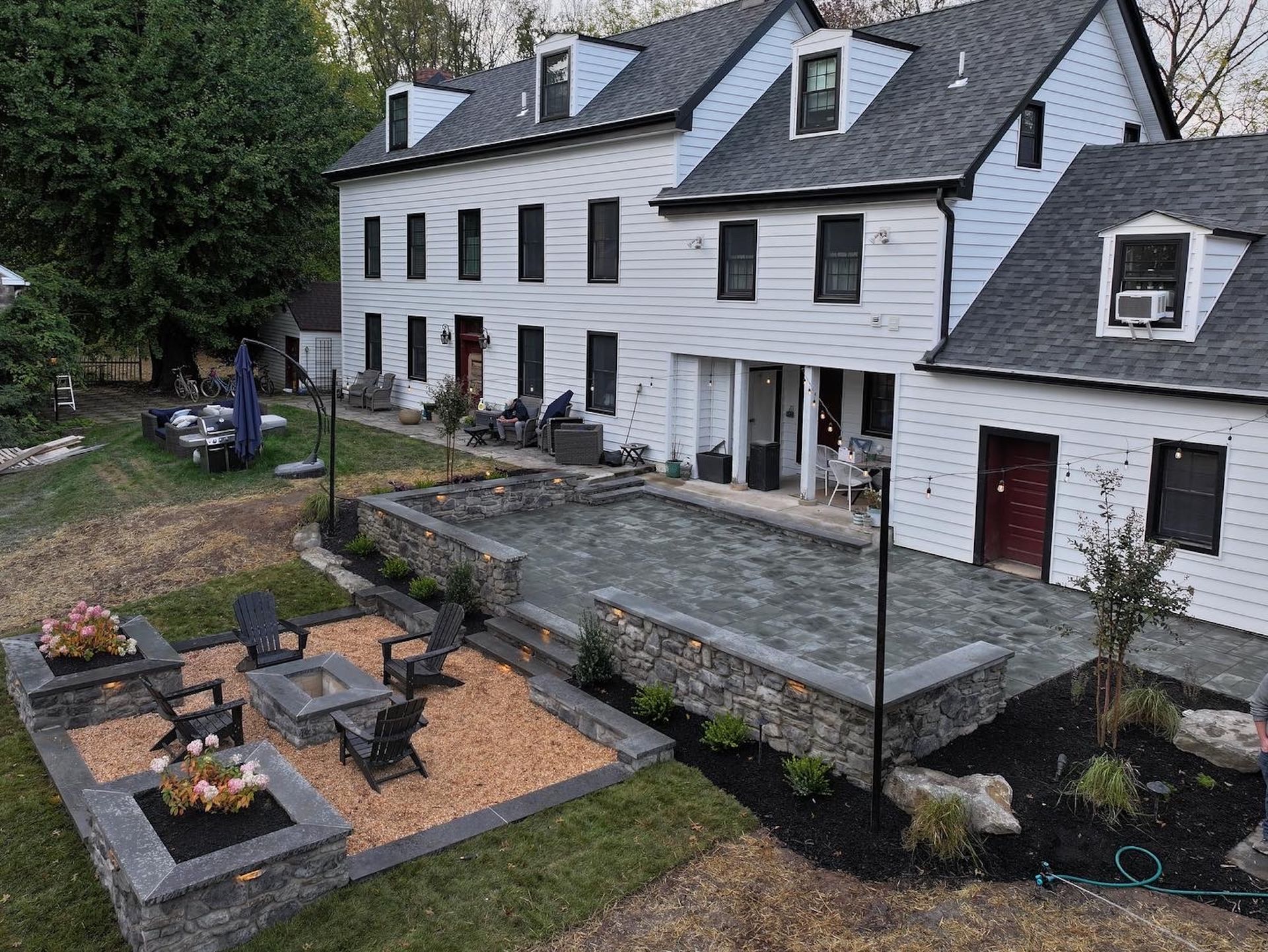 Exterior of white multi-story house with patio, fire pit, and landscaping.