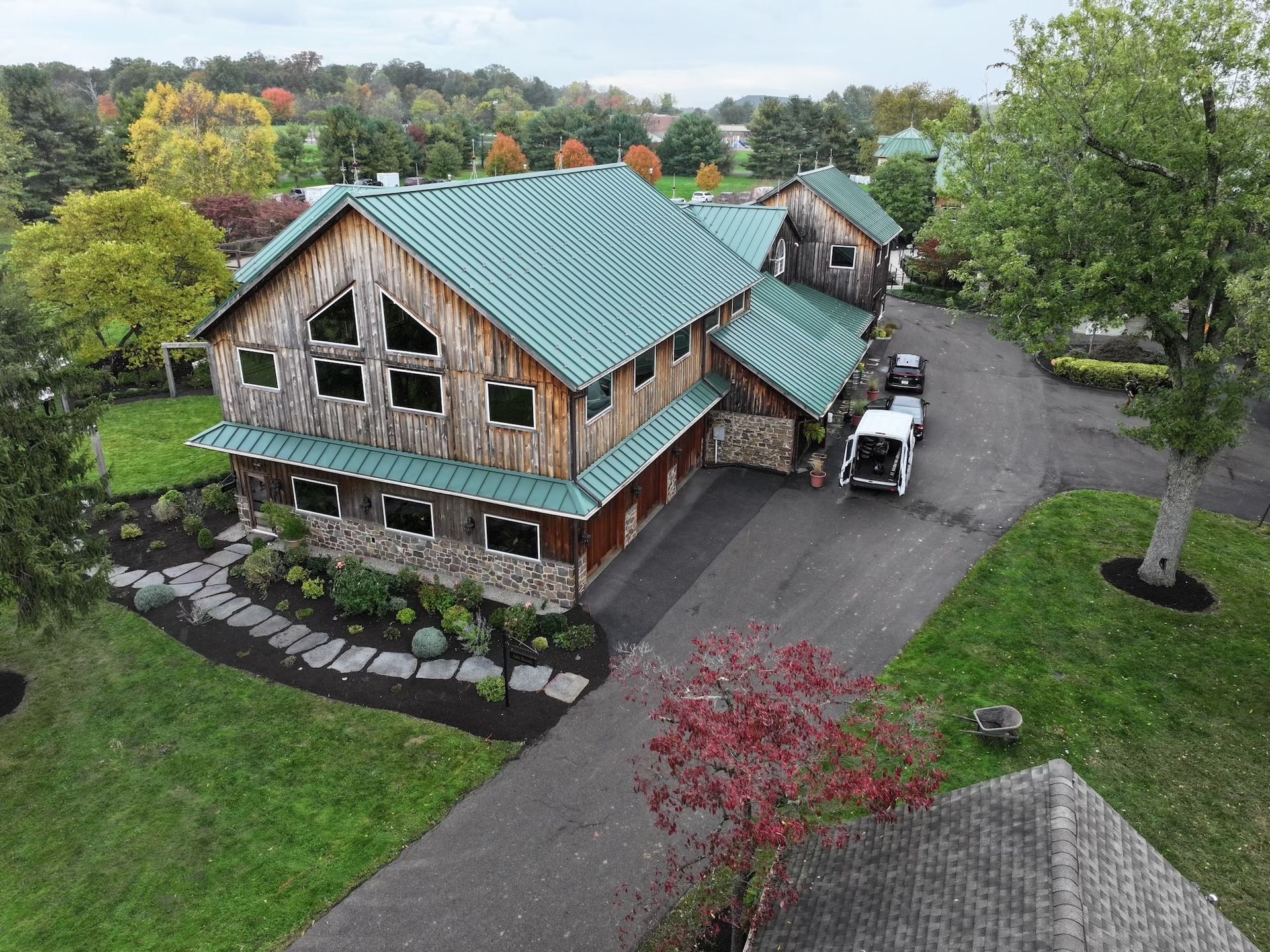 Rustic wooden building with green roof, long driveway, and surrounding trees.