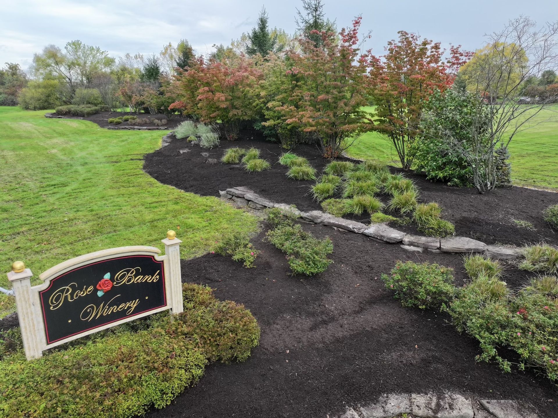 Sign for River Point Winery beside a landscaped garden with fall foliage.