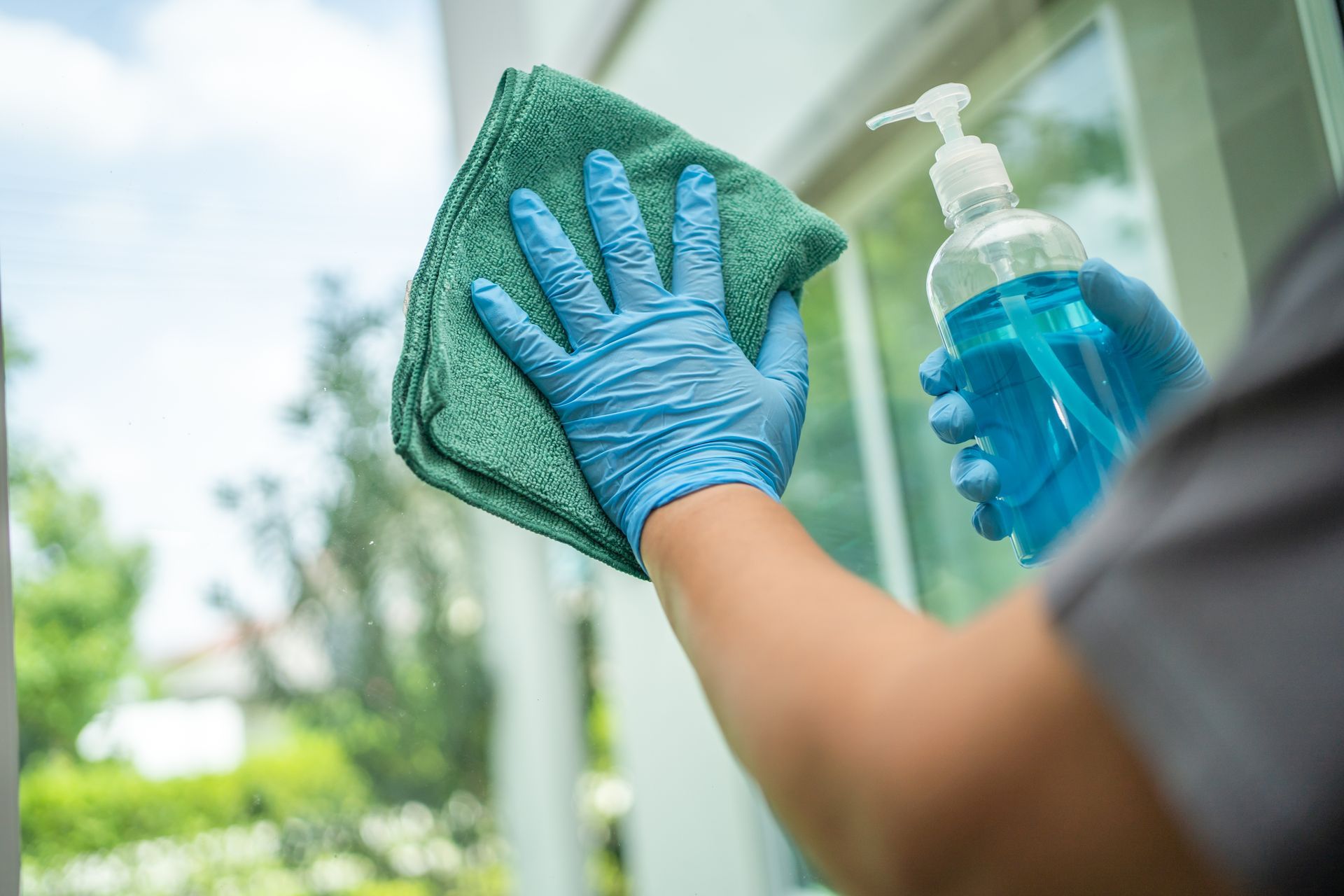 A person is cleaning a window with a cloth and a bottle of hand sanitizer.