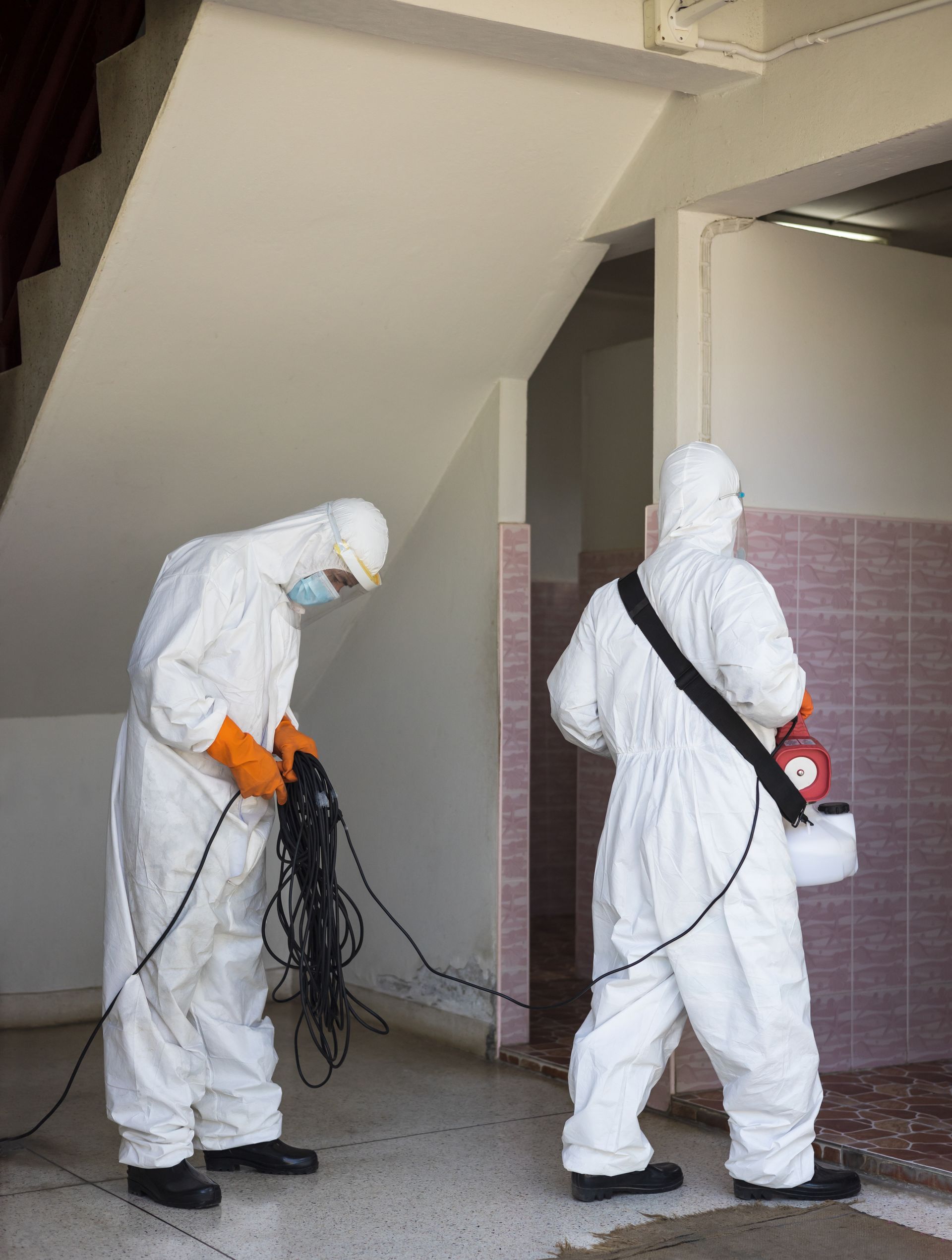 Two men in protective suits are disinfecting a room.