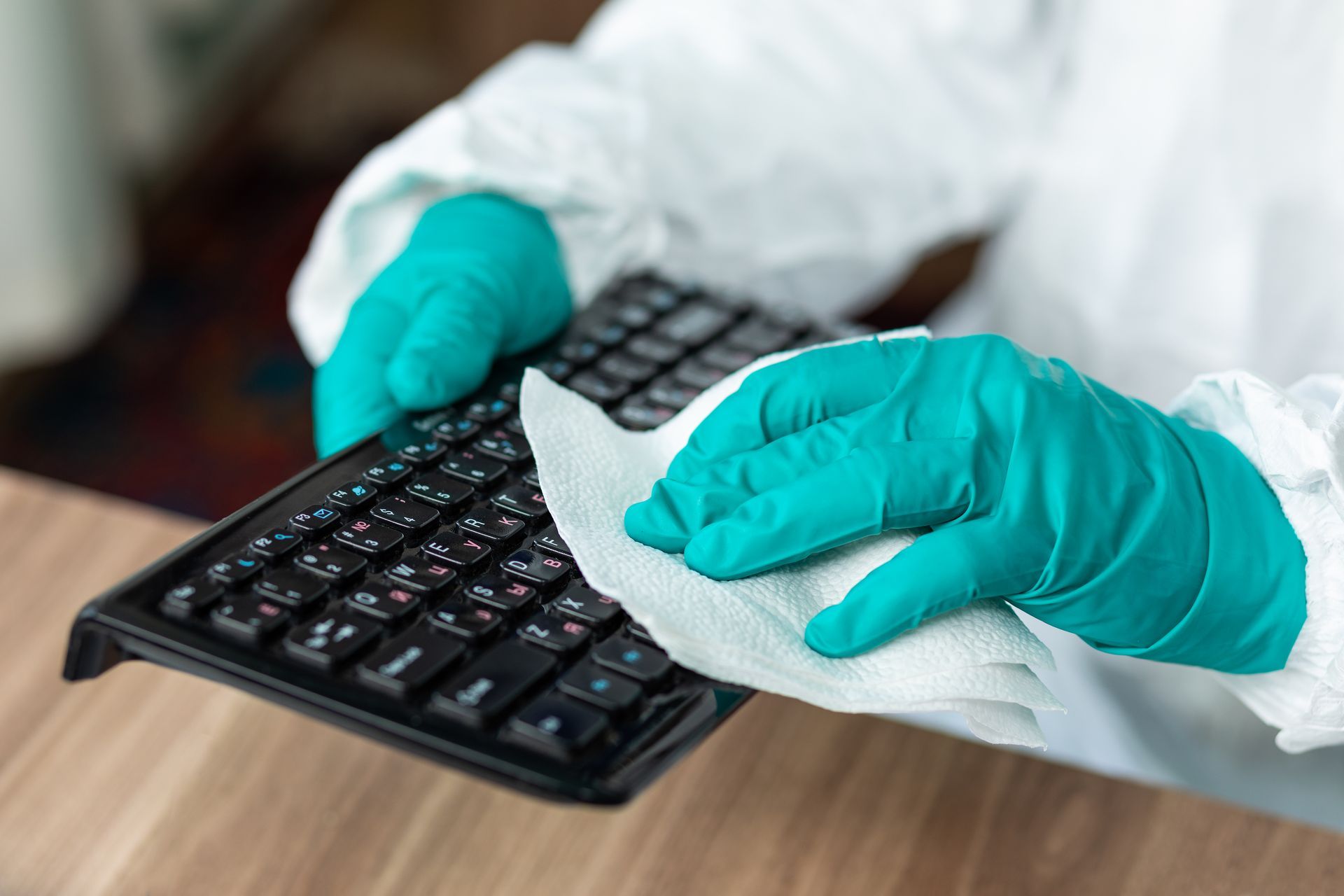 A person wearing gloves is cleaning a keyboard with a napkin.