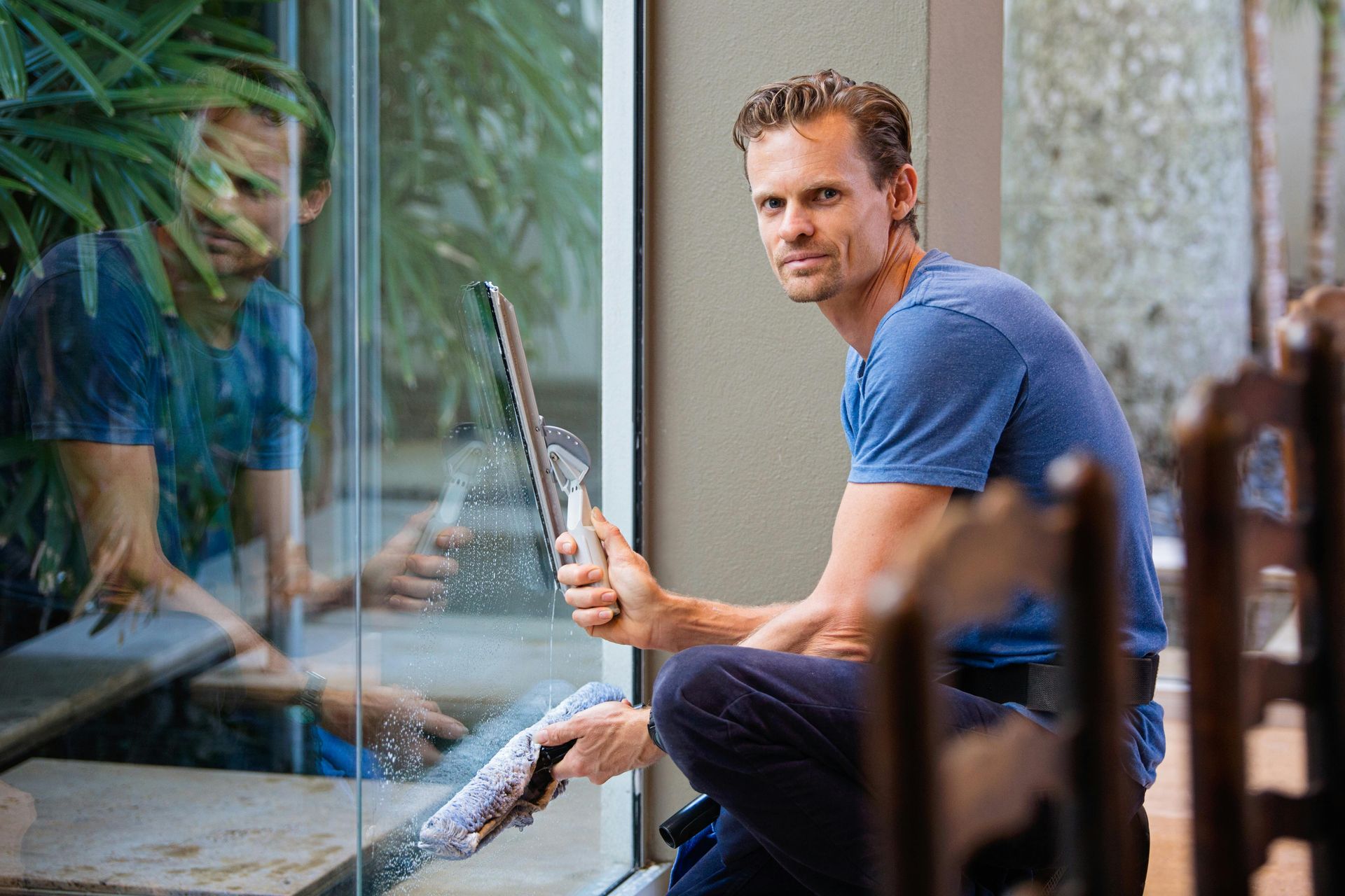 A man is kneeling down while cleaning a window with a squeegee.