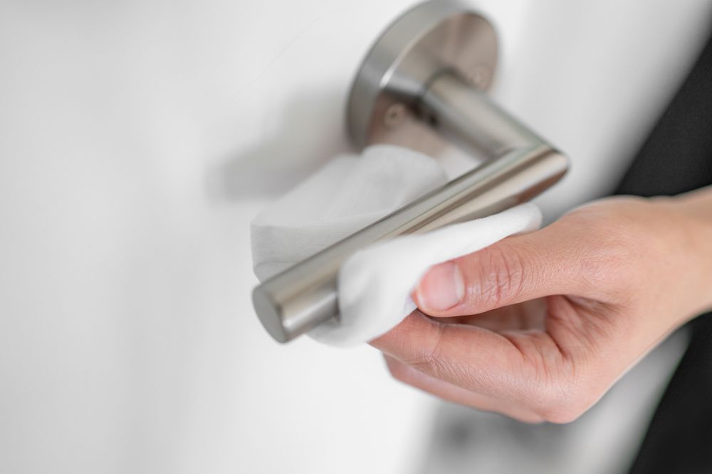 A person is cleaning a door handle with a wipe.
