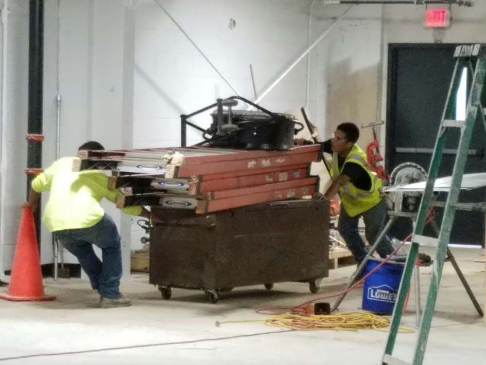 Two construction workers pushing a cart with a ladder in the background