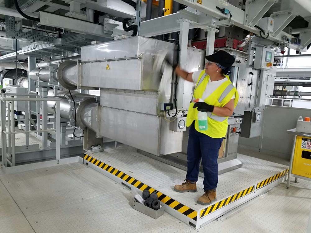 A man in a yellow vest is cleaning a machine in a factory.