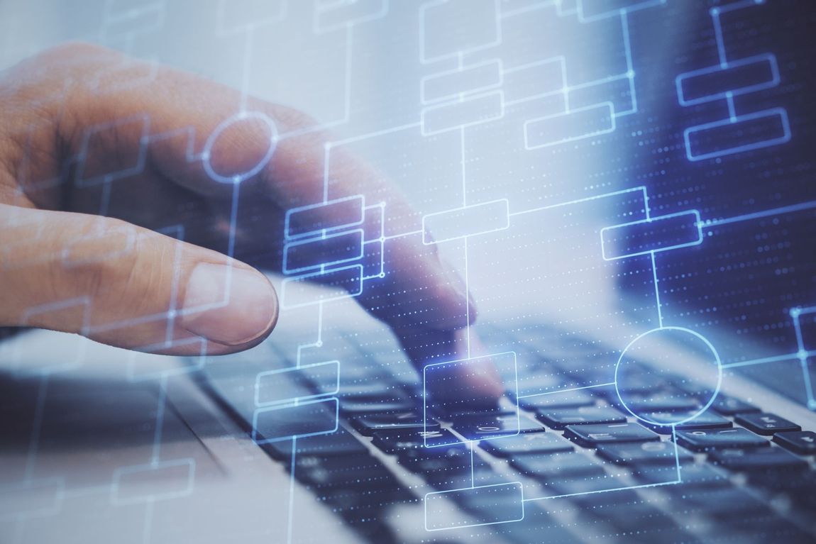 Hand typing on laptop keyboard with digital flowchart overlay.