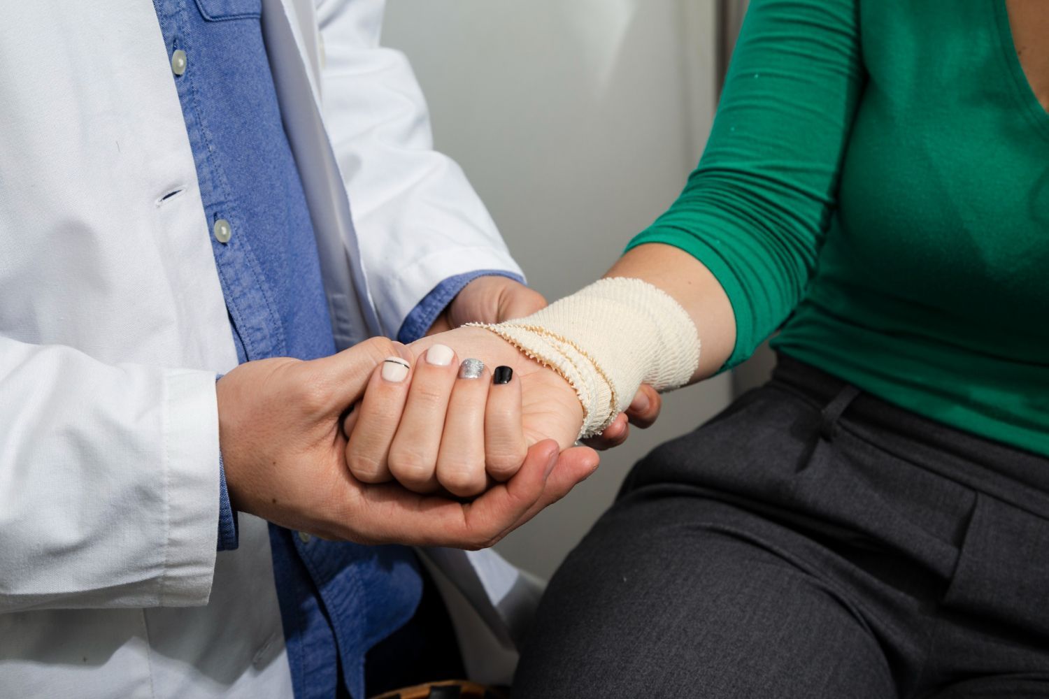 Doctor examining a woman's bandaged wrist in an examination room.