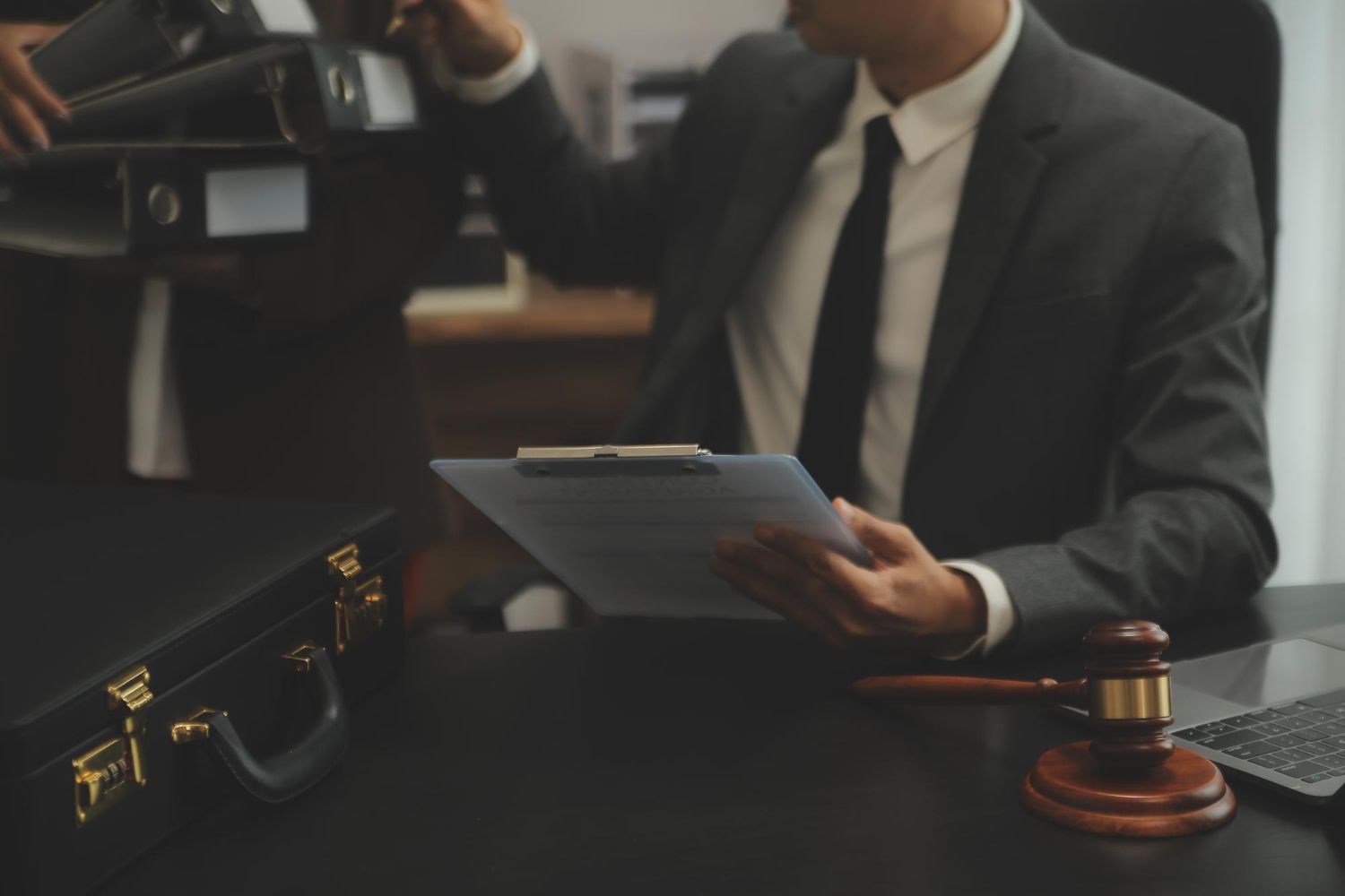 Lawyers in suits at a desk reviewing documents with a gavel and briefcase.
