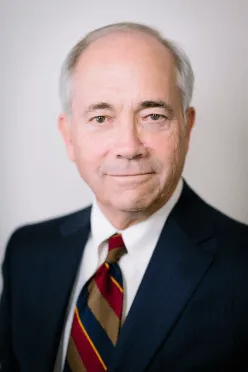 Man in a navy suit and tie, smiling at the camera.