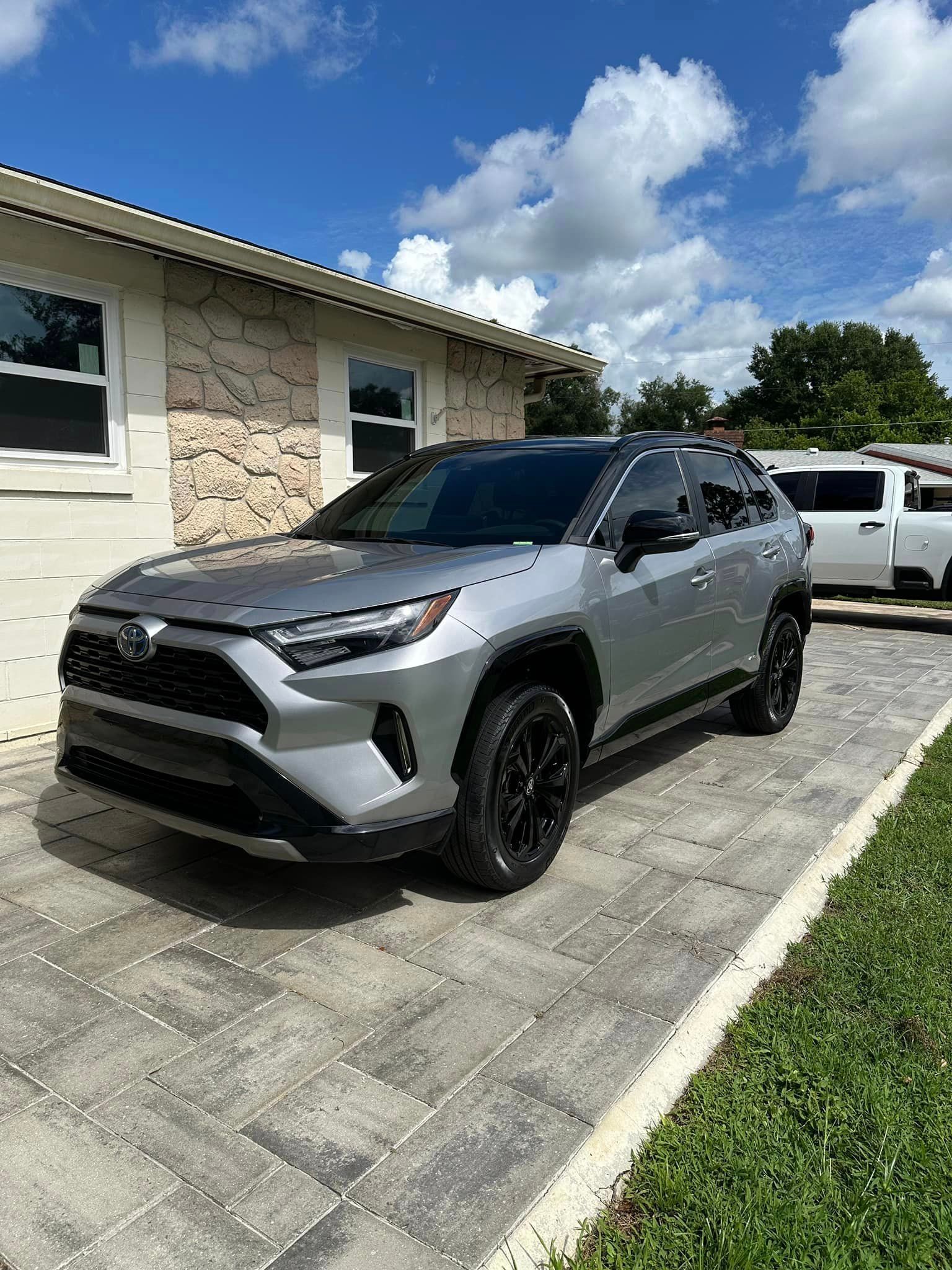 A silver toyota rav4 is parked in a driveway in front of a house.