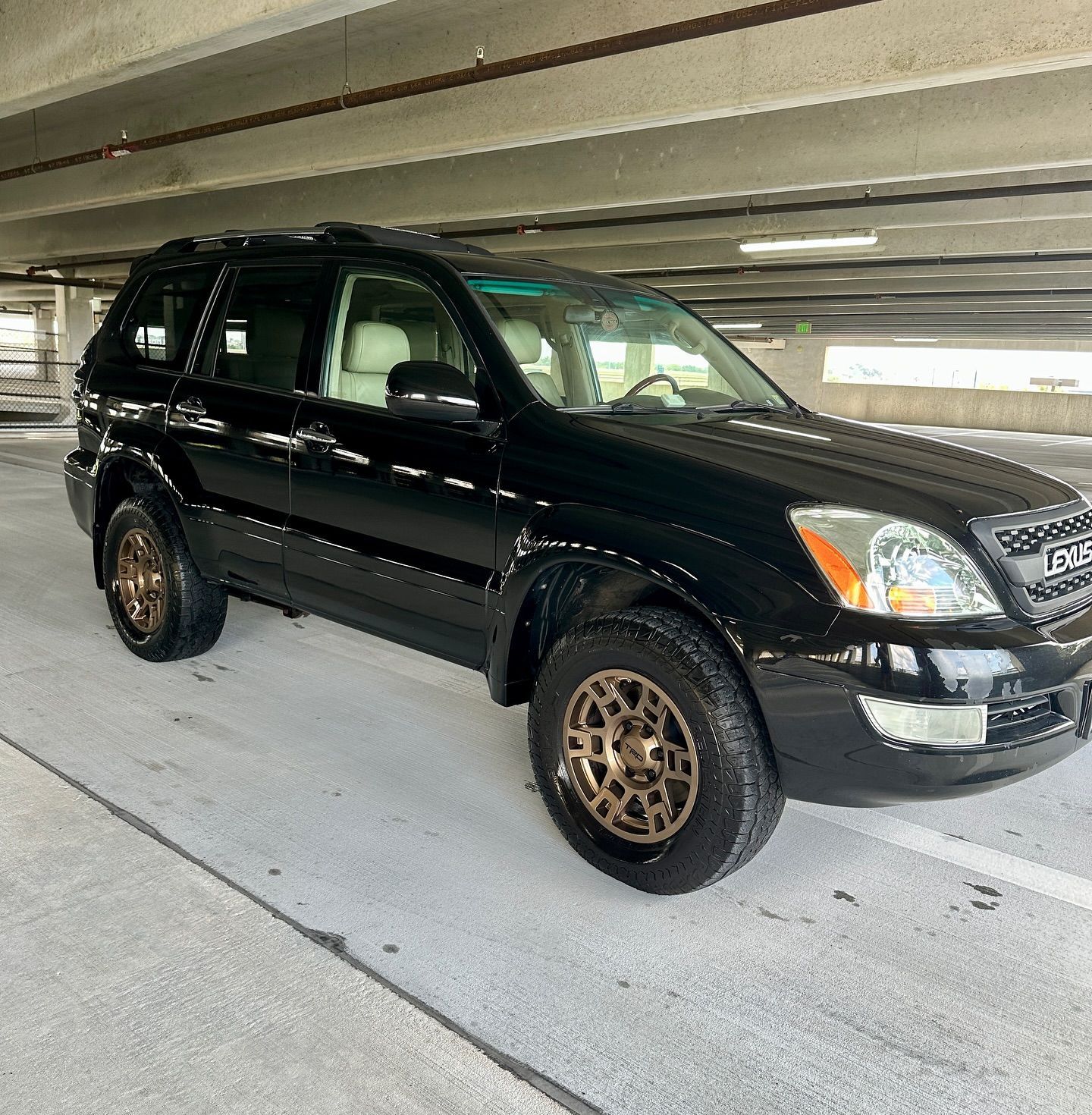 A black suv is parked in a parking garage under a bridge.