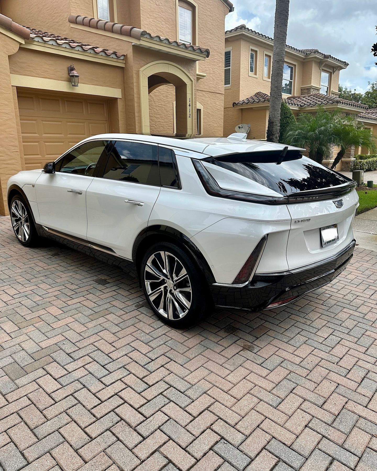 A white car is parked in front of a house on a brick driveway.