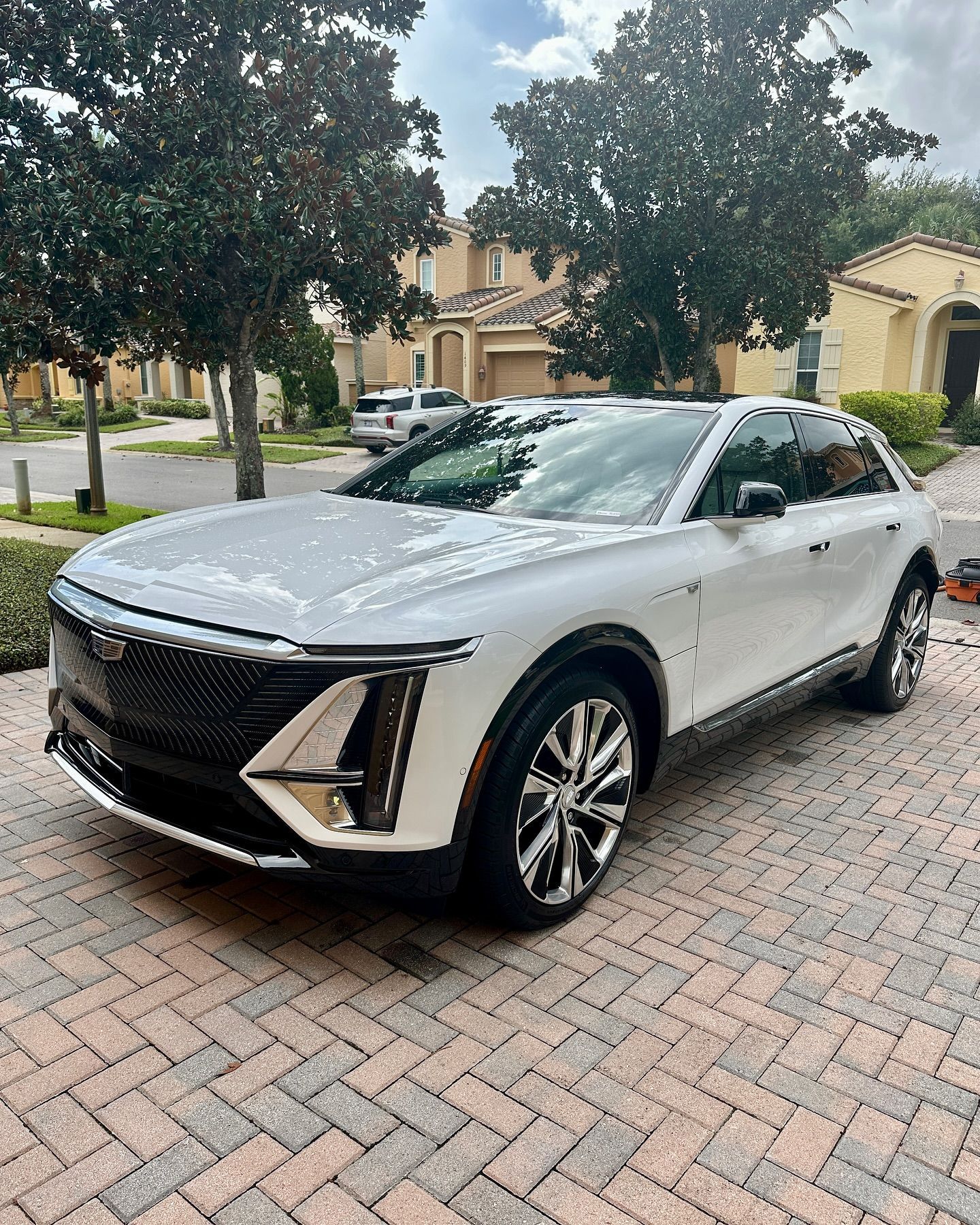 A white car is parked on a brick driveway in front of a house.