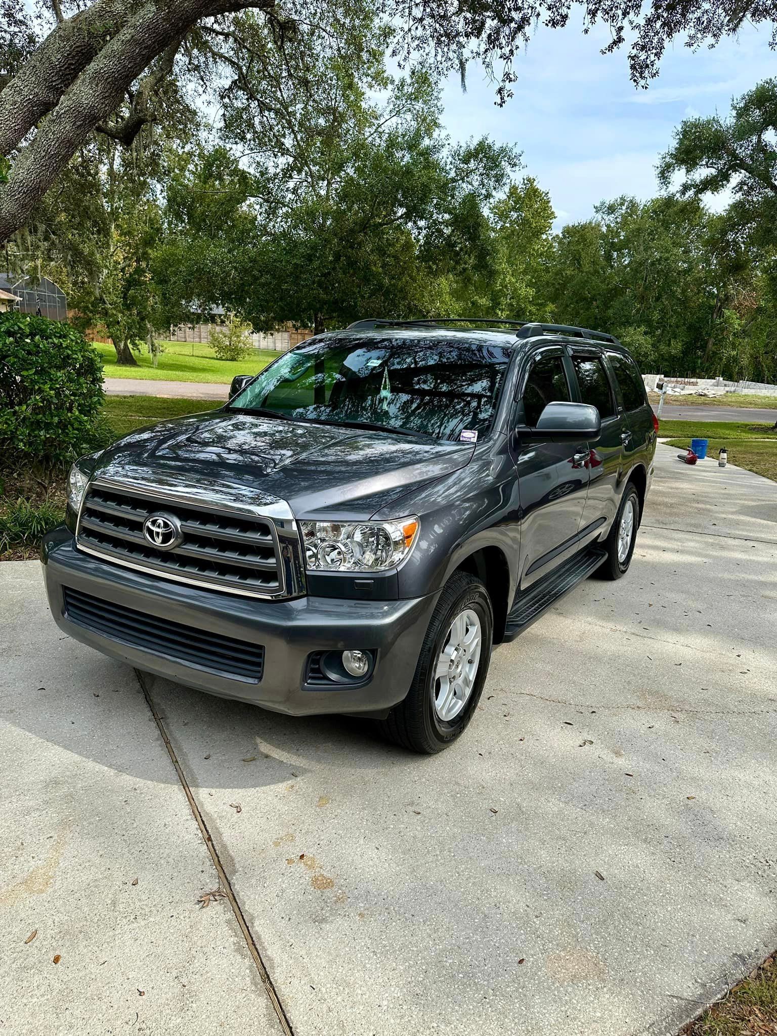 A toyota sequoia is parked on a sidewalk next to a tree.