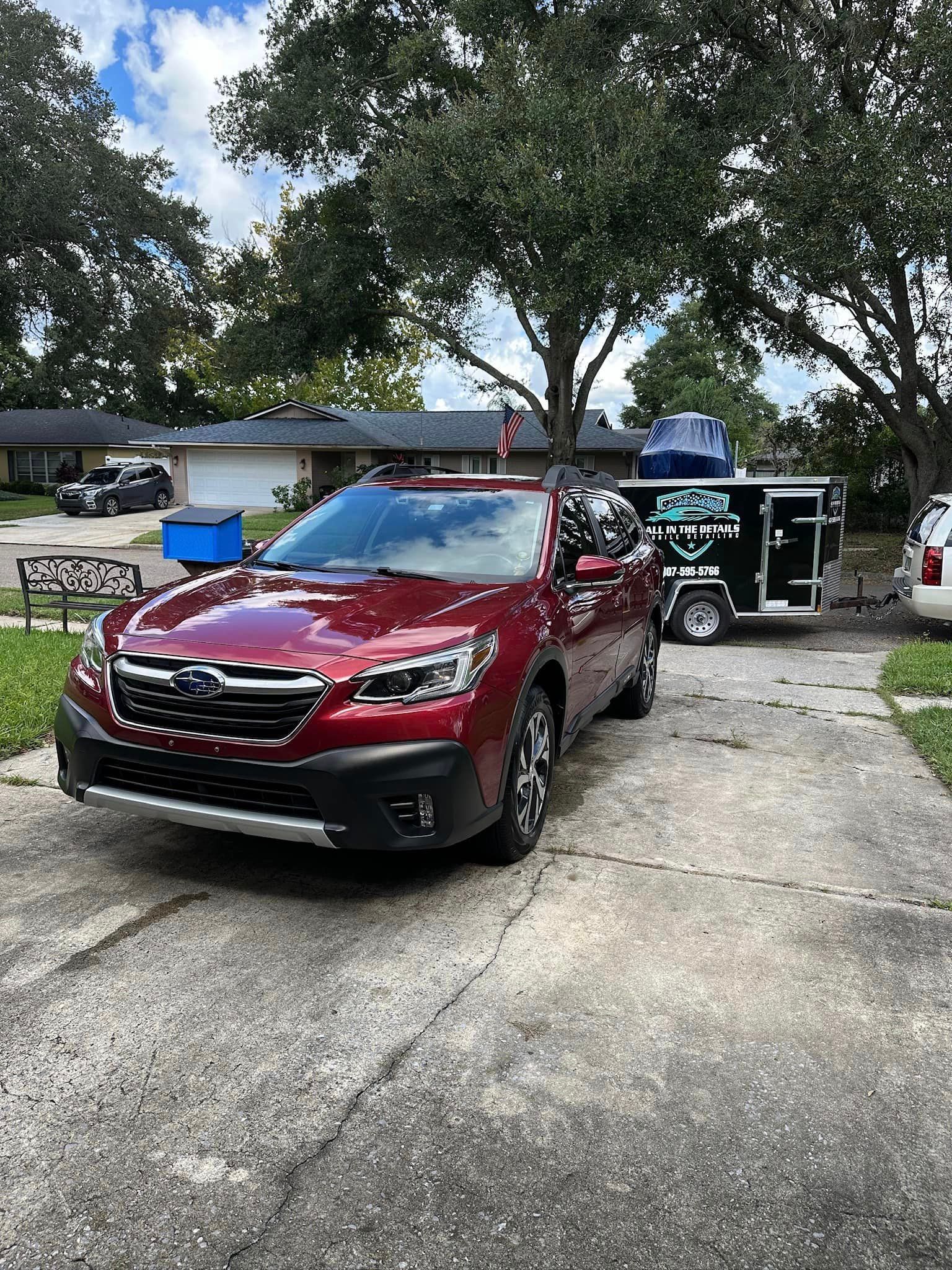 A red car is parked in a driveway next to a trailer.