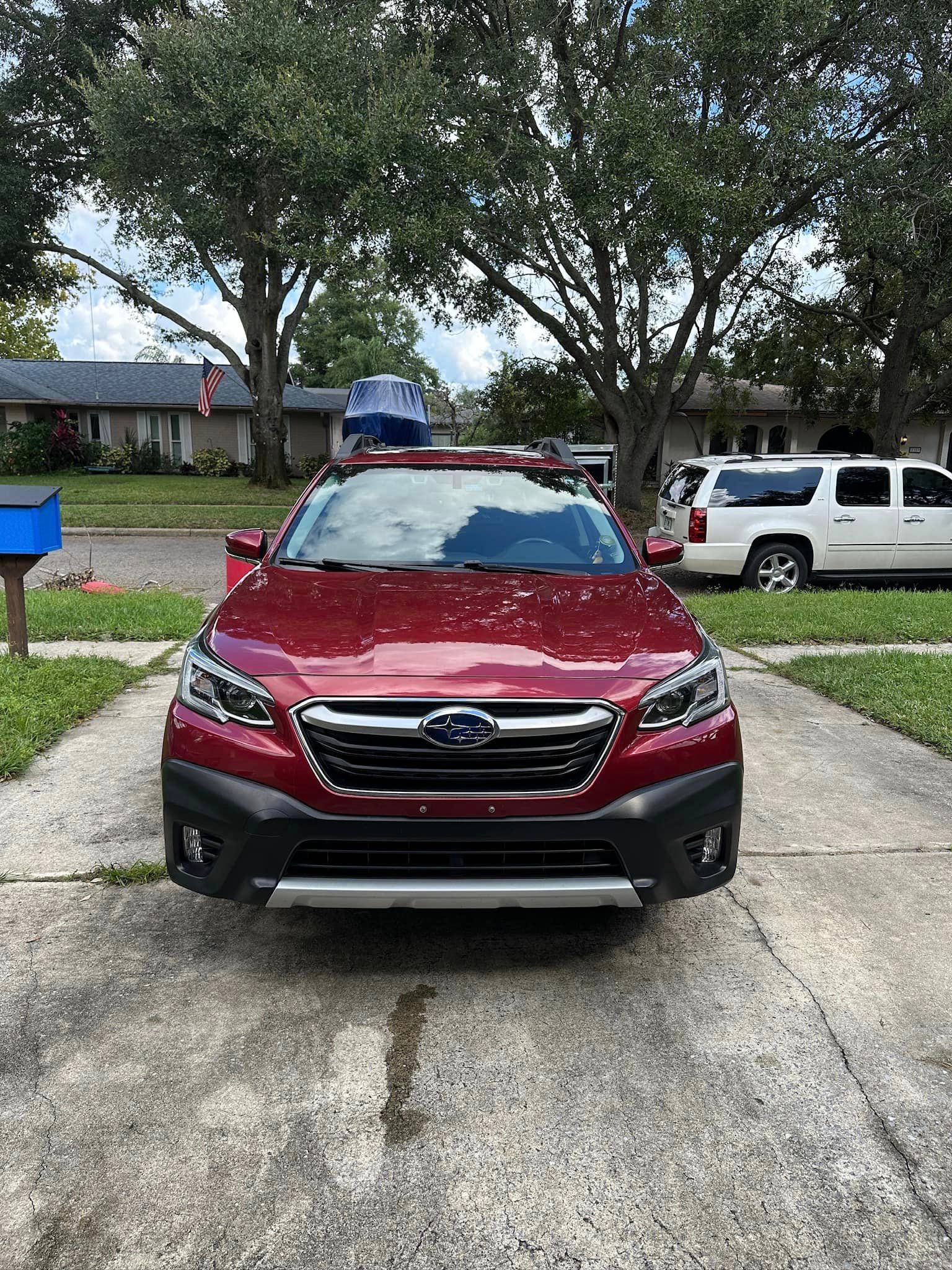 A red subaru outback is parked in a driveway.