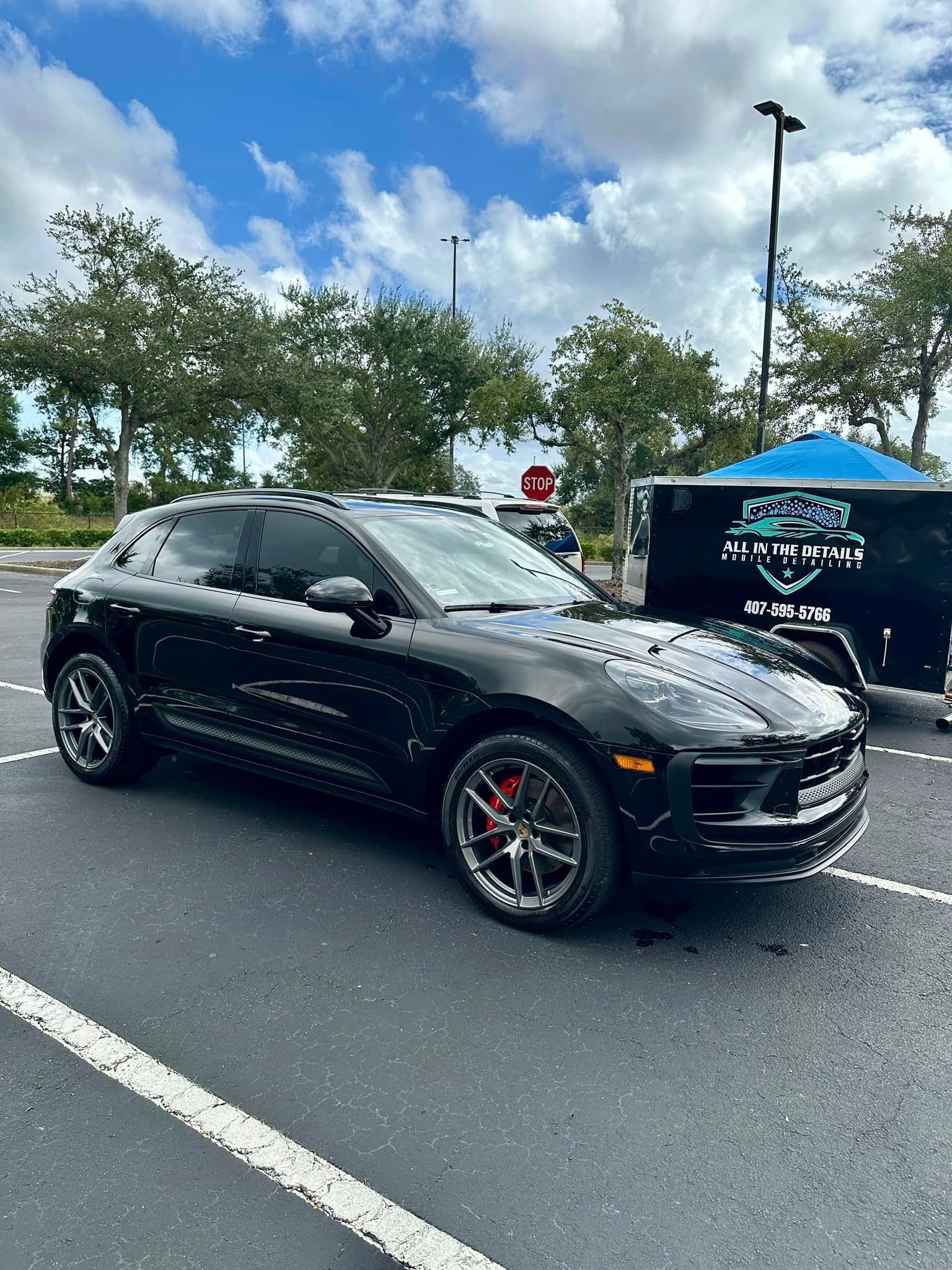 A black porsche macan is parked in a parking lot next to a trailer.