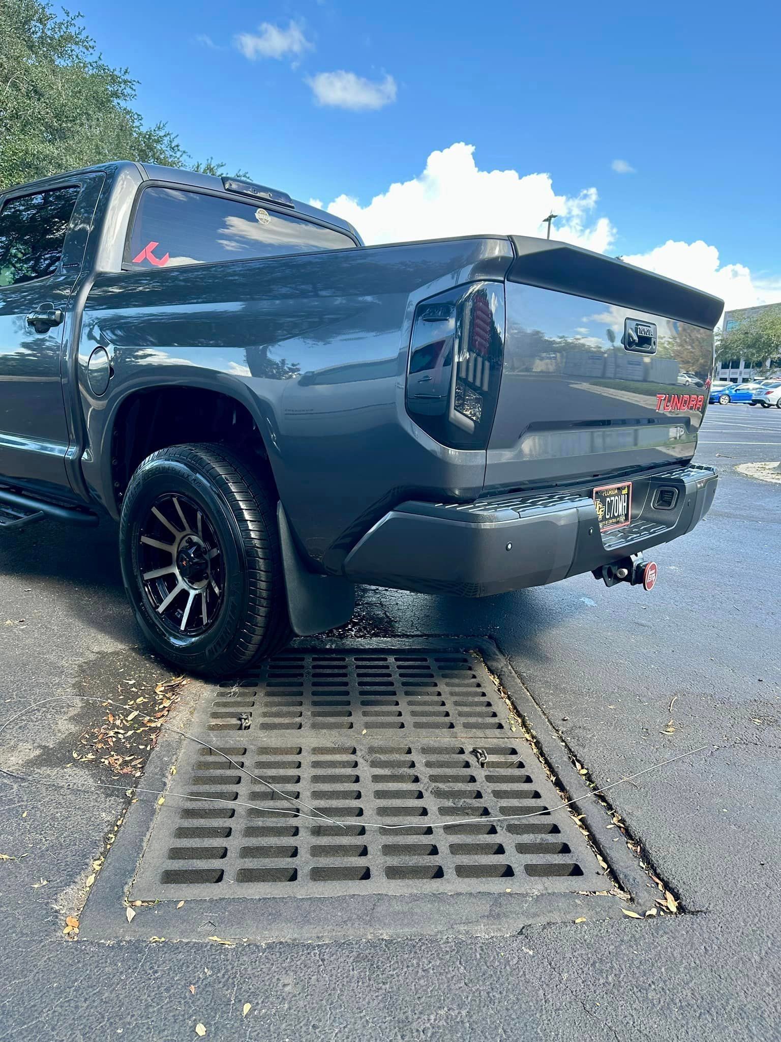 A black truck is parked on the side of the road next to a drain.