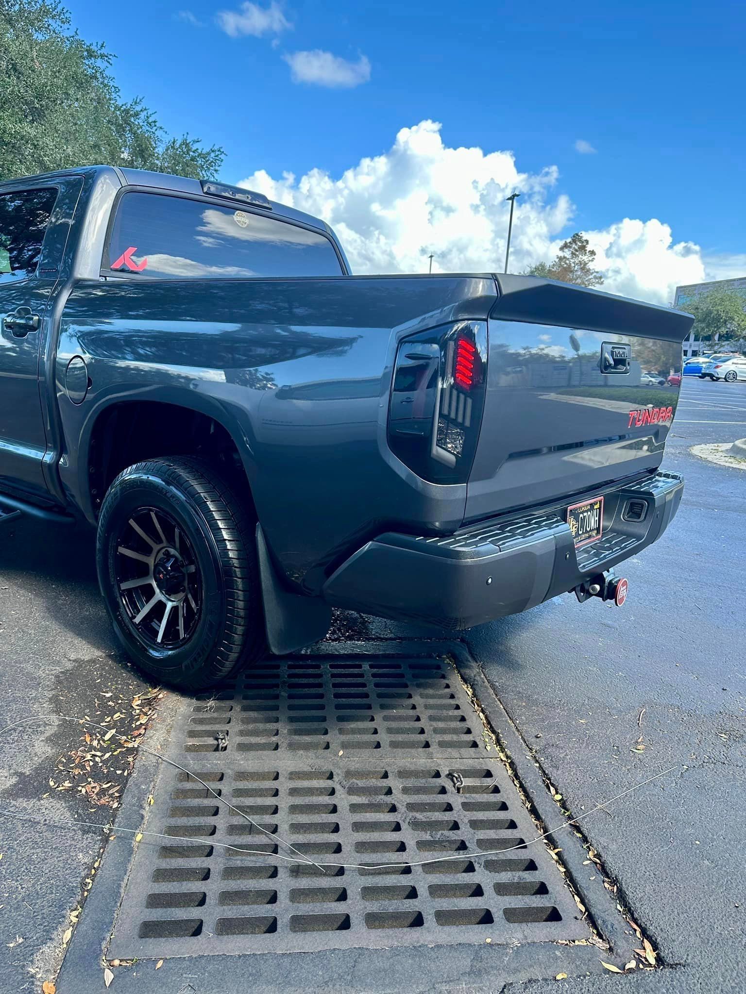 A black truck is parked next to a drain in a parking lot.