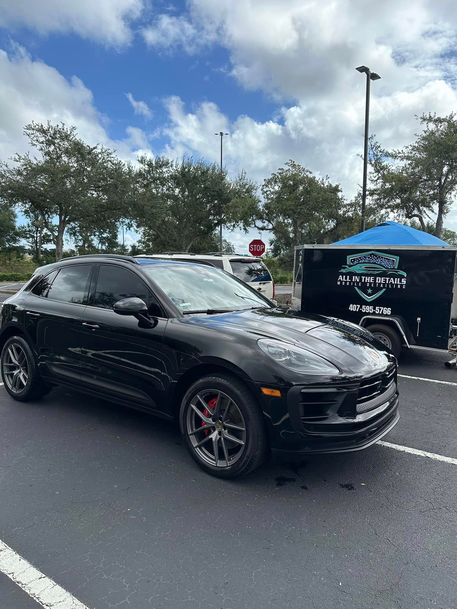 A black porsche macan is parked in a parking lot next to a trailer.