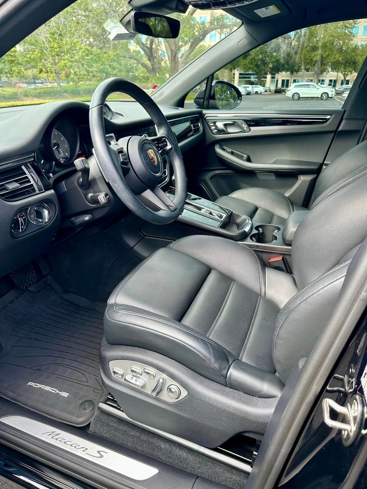 The interior of a black porsche macan s with the door open.