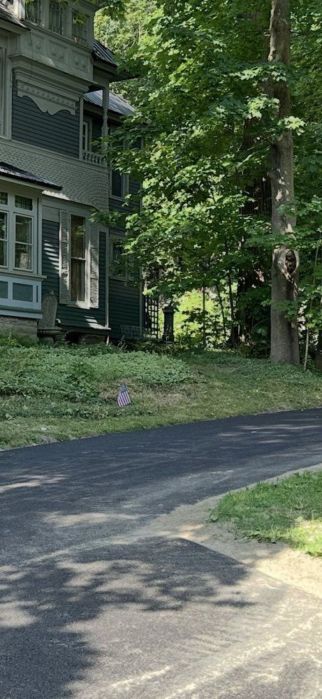 Dark, tree-lined road next to a Victorian-style house with green paint and decorative trim.