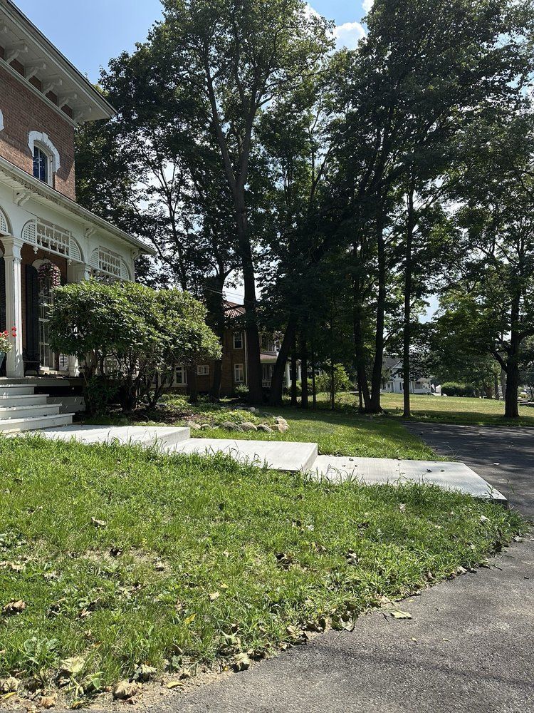 Exterior of a white-trimmed brick building. A stone walkway leads to the entrance, with green grass and trees in the 