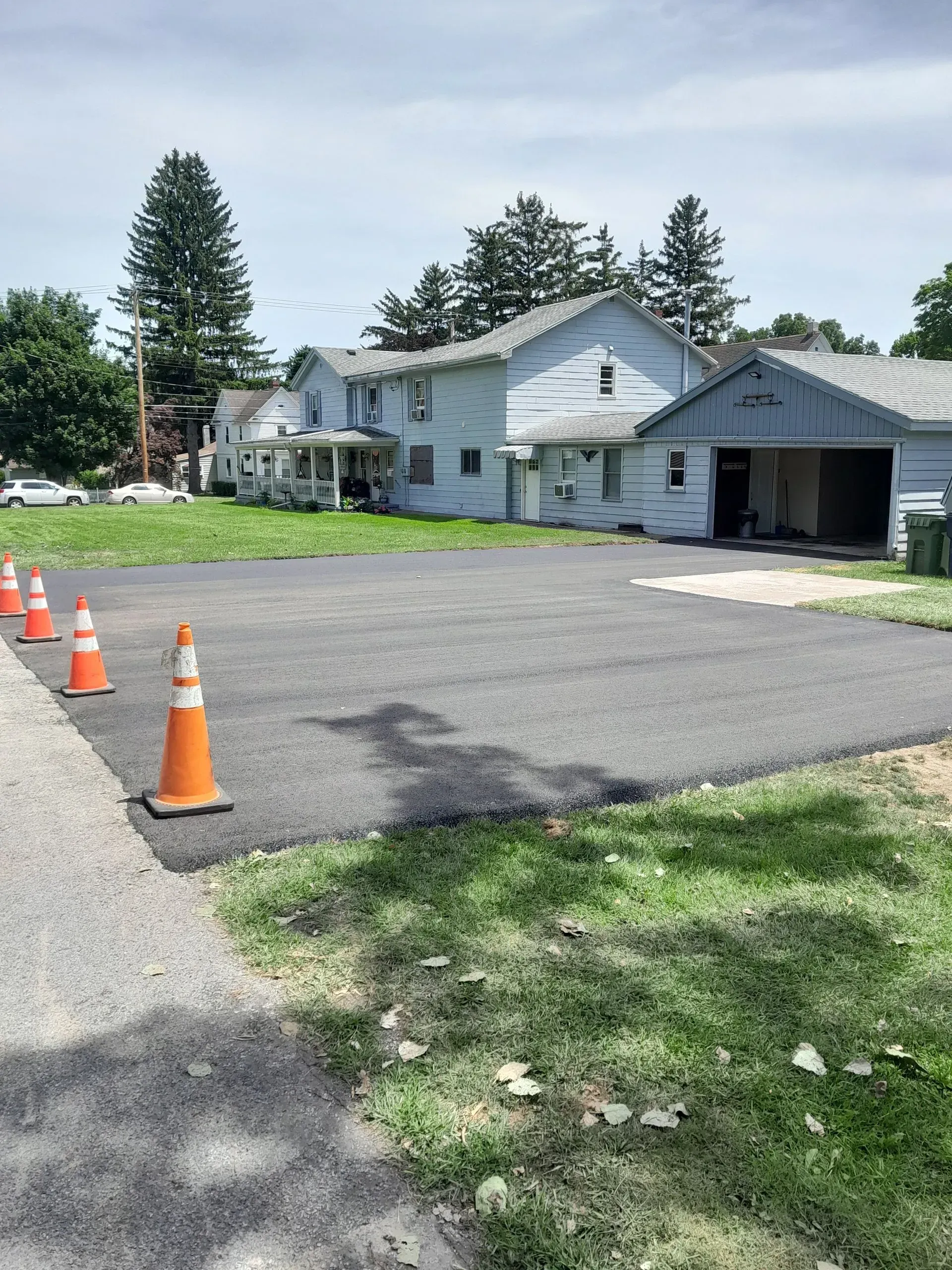 Newly paved asphalt area with orange safety cones, next to a weathered two-story building.