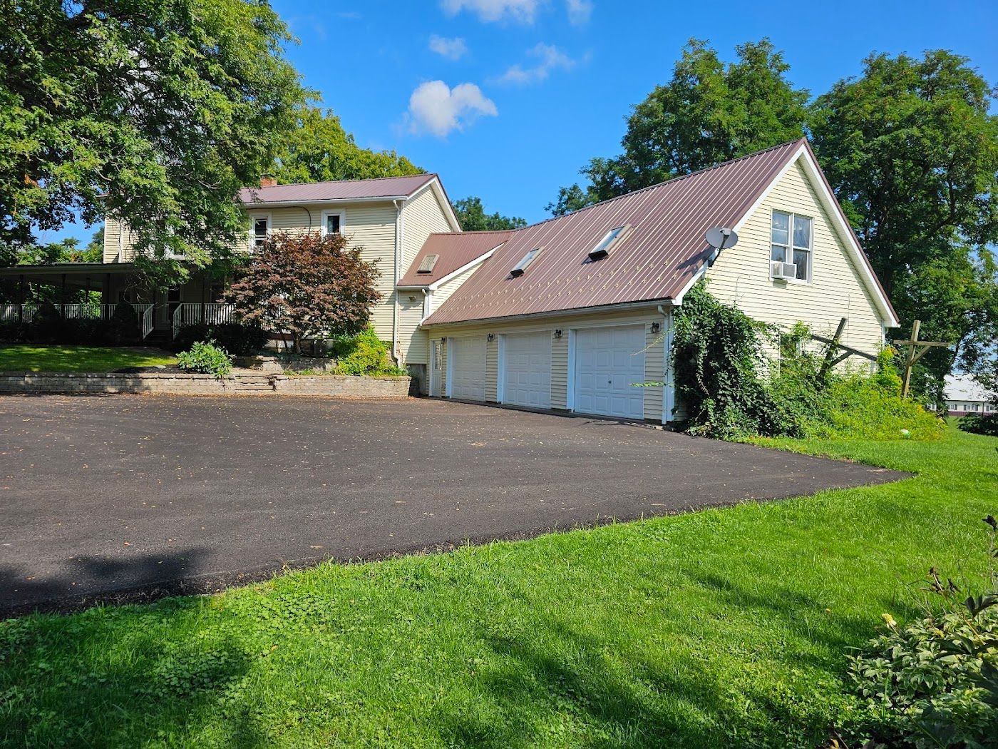 House with three-car garage and asphalt driveway on a grassy hillside under a blue sky.