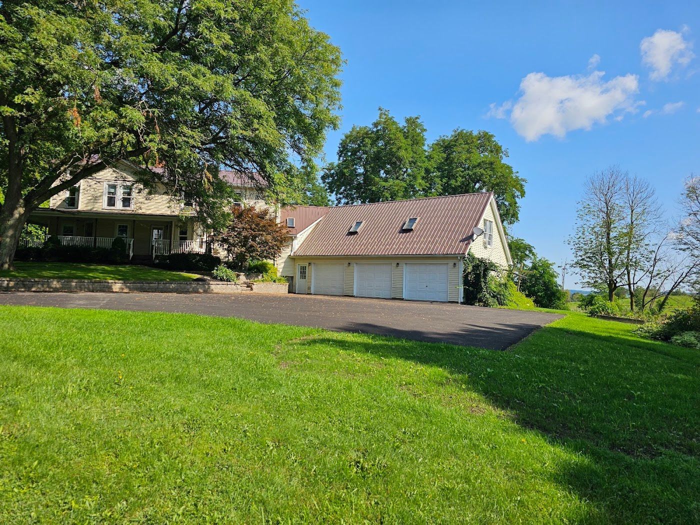 A two-story stone house with a three-car garage on a grassy hill under a blue sky.
