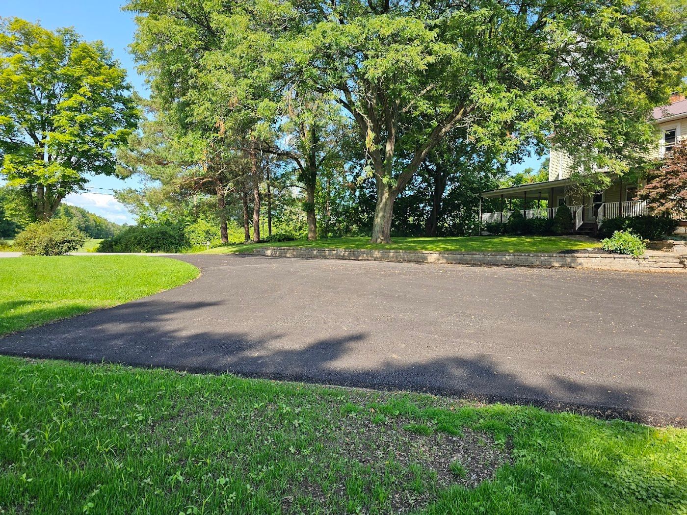 Asphalt driveway curves through a green lawn, leading to a house in the distance with trees.