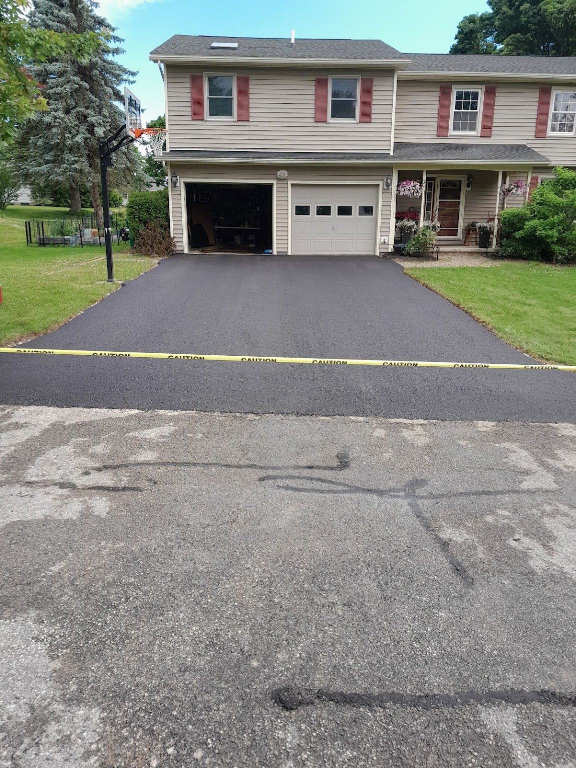 Freshly paved driveway in front of a two-story home, separated by caution tape from the old cracked pavement.