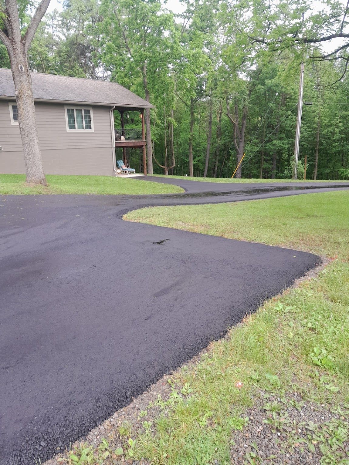 Asphalt driveway curving towards a house, with grass on the side and trees in the background.