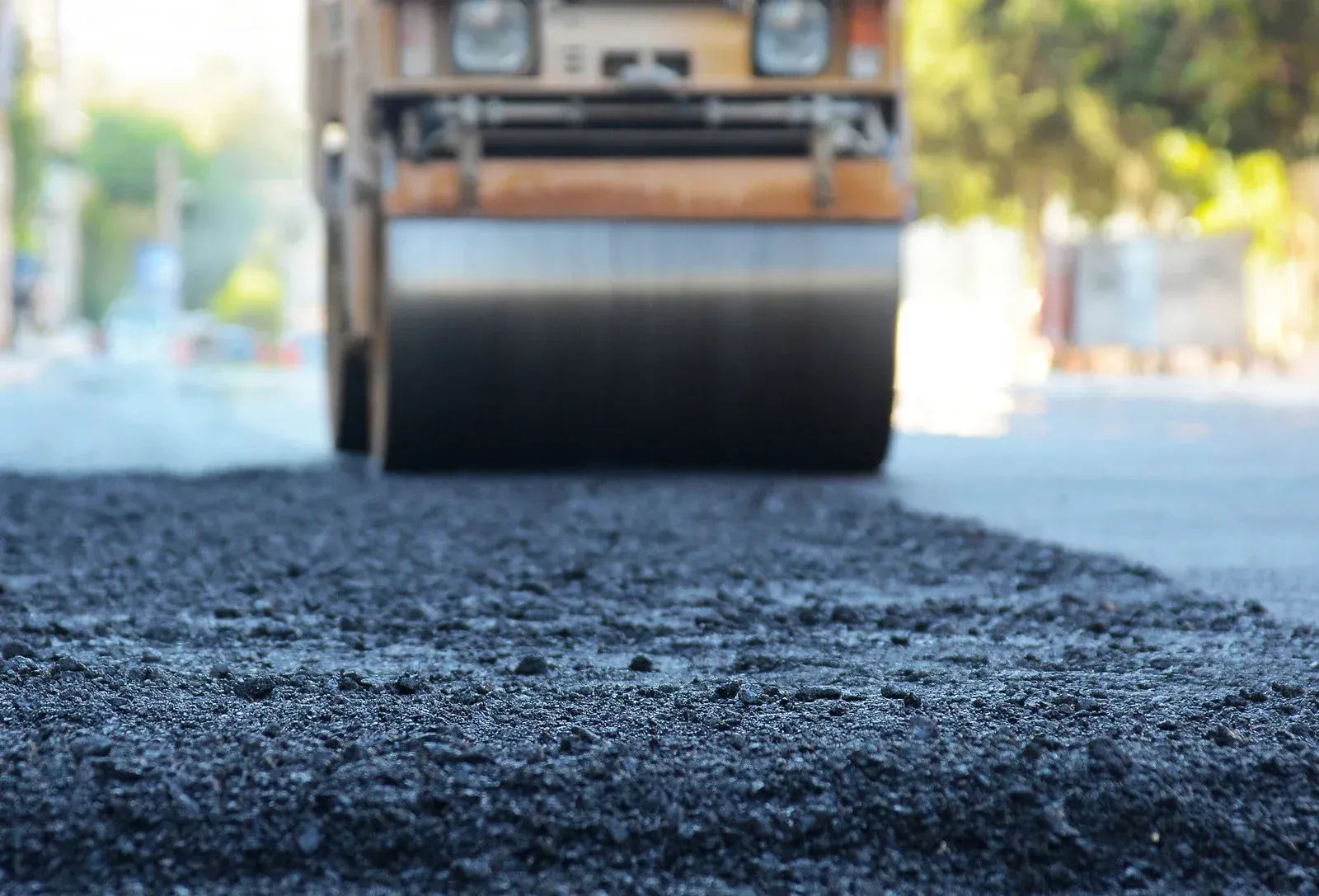Road roller compacting fresh asphalt on a city street.