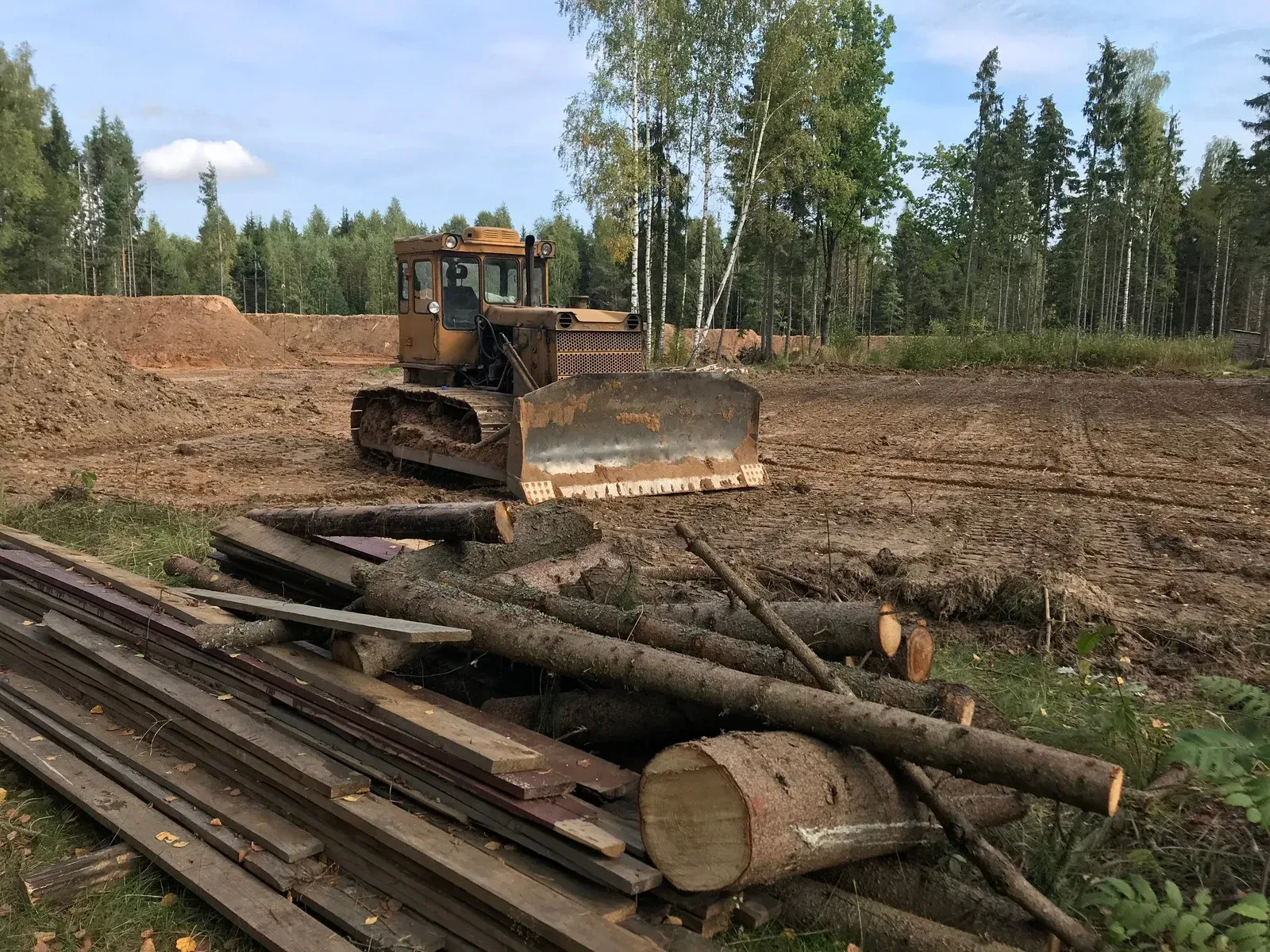 Dozer clearing land in a forest area. Logs and wood scraps in foreground, trees in background.
