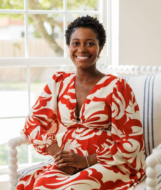 A woman is sitting at a desk with a laptop and a vase of flowers.