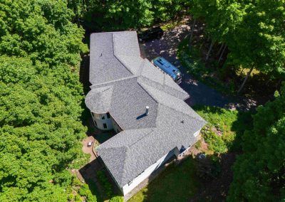 An aerial view of a house with a roof that is surrounded by trees.