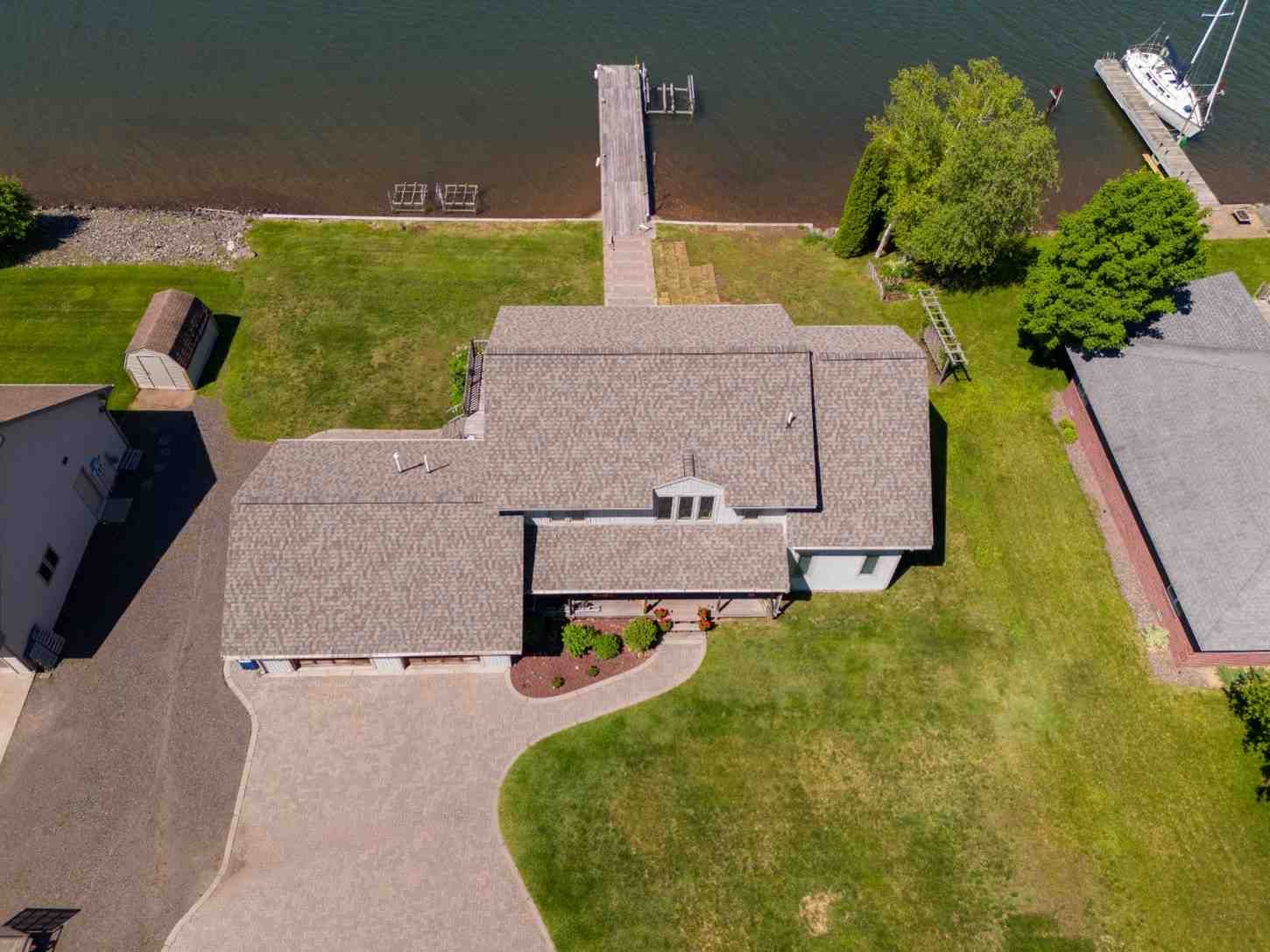 Aerial view of a house with a dock on a lake. The house has a gray roof and a long driveway.