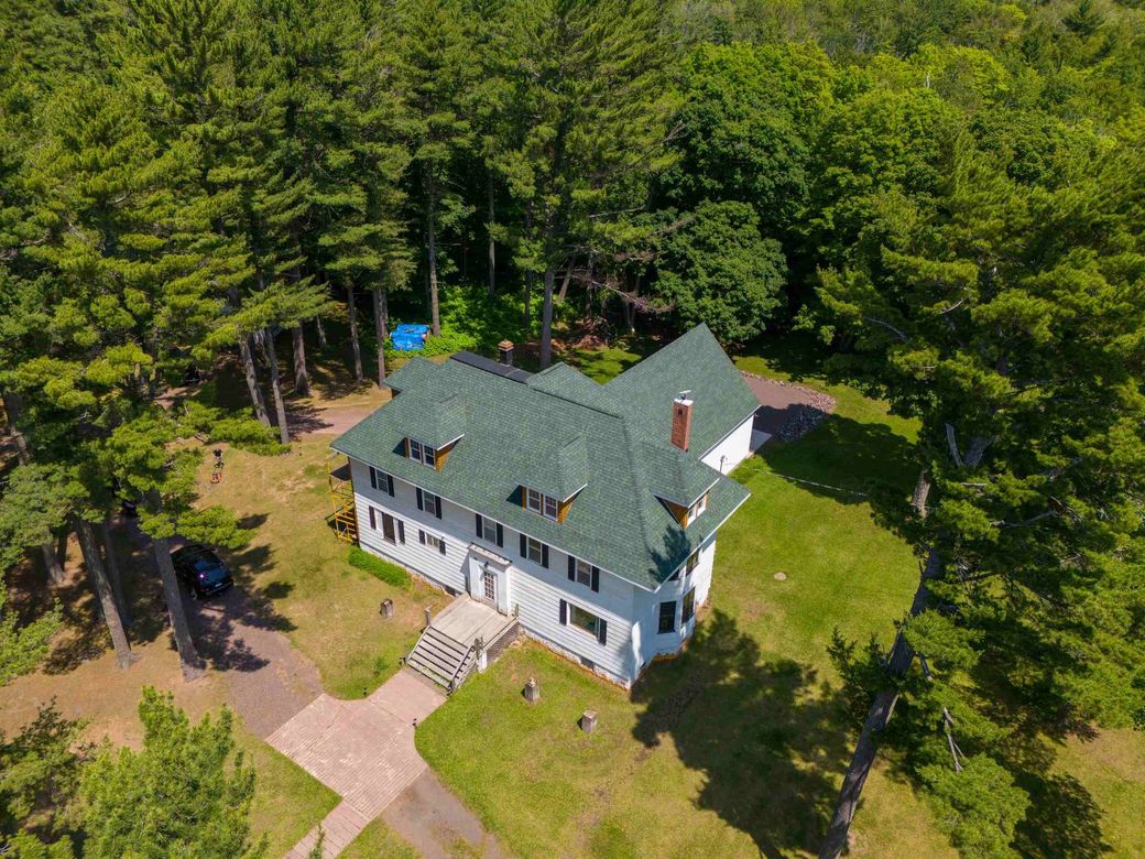 An aerial view of a white house with a green roof in the middle of a forest.