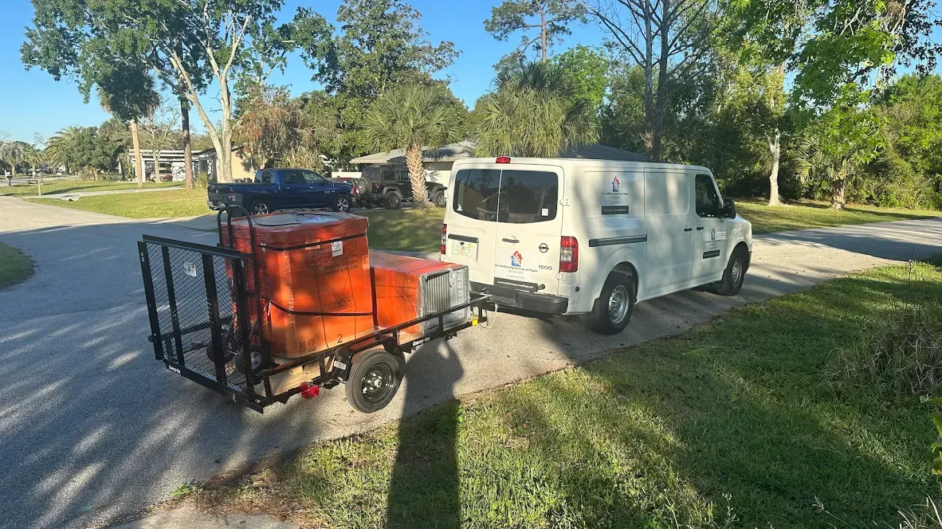 A white van towing a small black trailer with large orange equipment is parked on a suburban street.